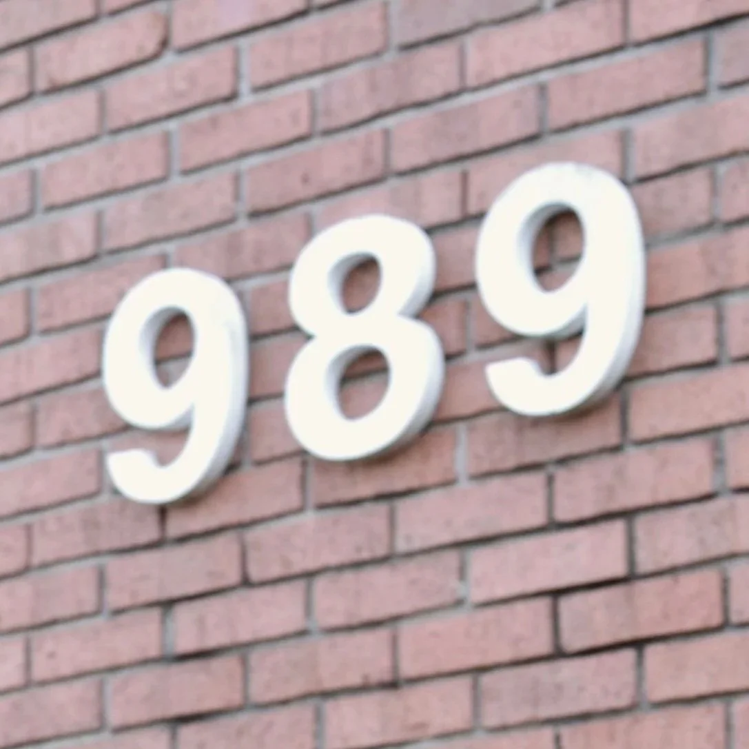 White house number 989 mounted on a red brick exterior wall.