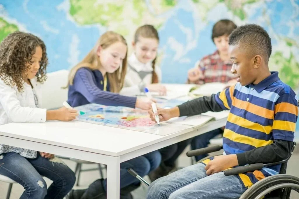 Five children sitting around a table, writing on a colorful board game, with a world map in the background.