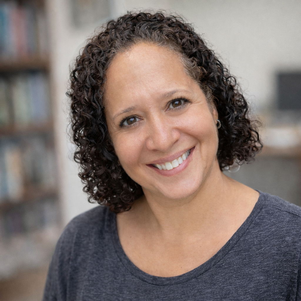 A woman with curly dark hair and a gray shirt, smiling at the camera.