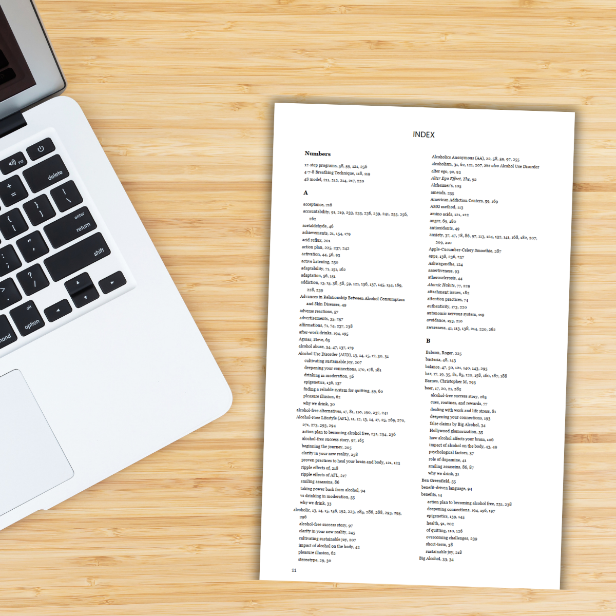Laptop on a wooden desk with a printed index or reference sheet beside it.