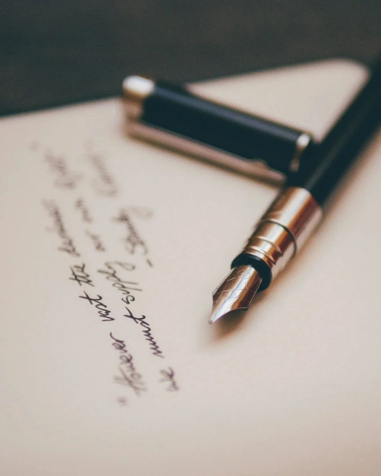 Un bolígrafo de color plateado y negro sobre una hoja con escritura manuscrita, y un cuaderno o agenda cerrada en el fondo.