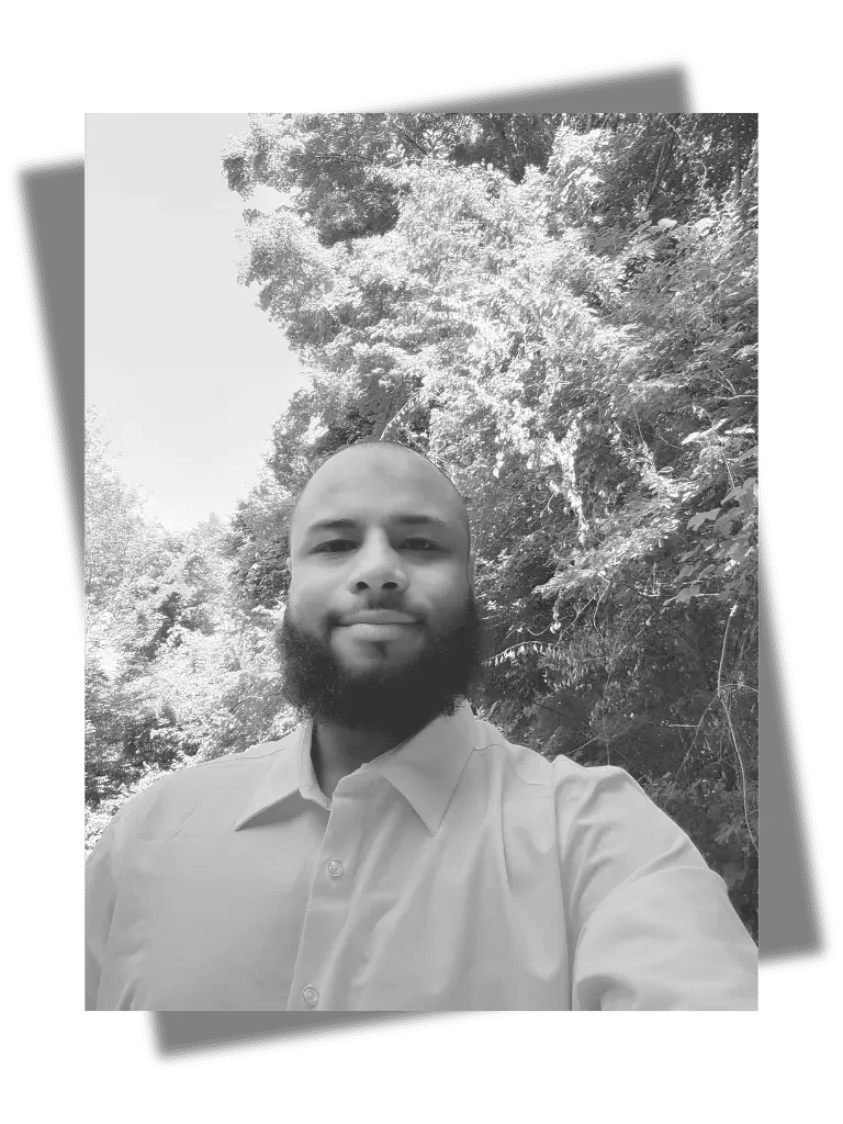 Black-and-white selfie of a man with a beard wearing a collared shirt, standing outdoors in front of trees.
