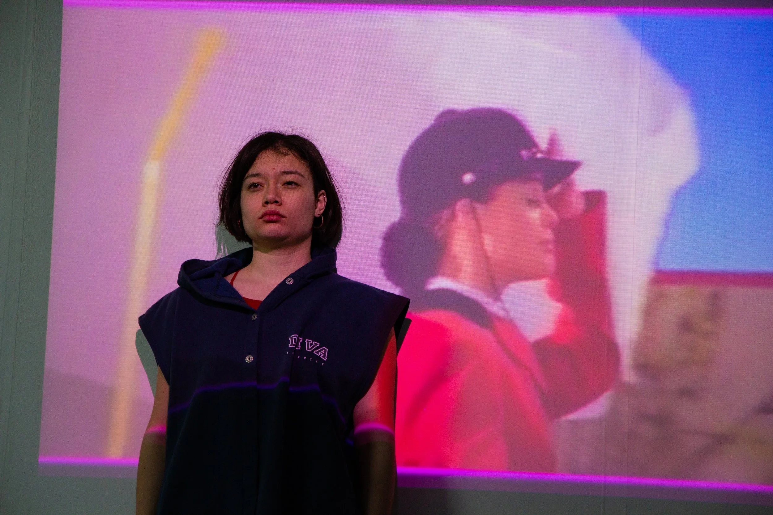 Une jeune fille avec une veste noire, debout devant un écran de projection, où l’on voit une autre fille en uniforme de navigation, portant une casquette, en train de regarder à travers des jumelles.