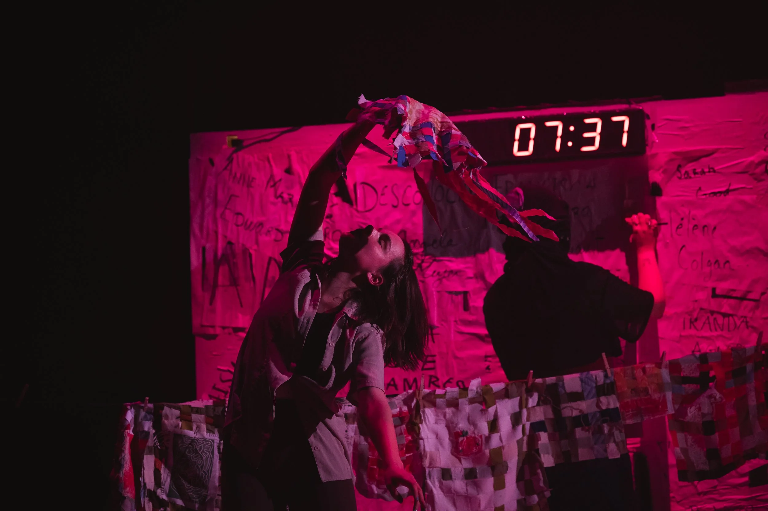 Une scène théâtrale sombre avec deux femmes  dans un décor coloré en rose avec un tableau de bord numérique affichant 07:37.
