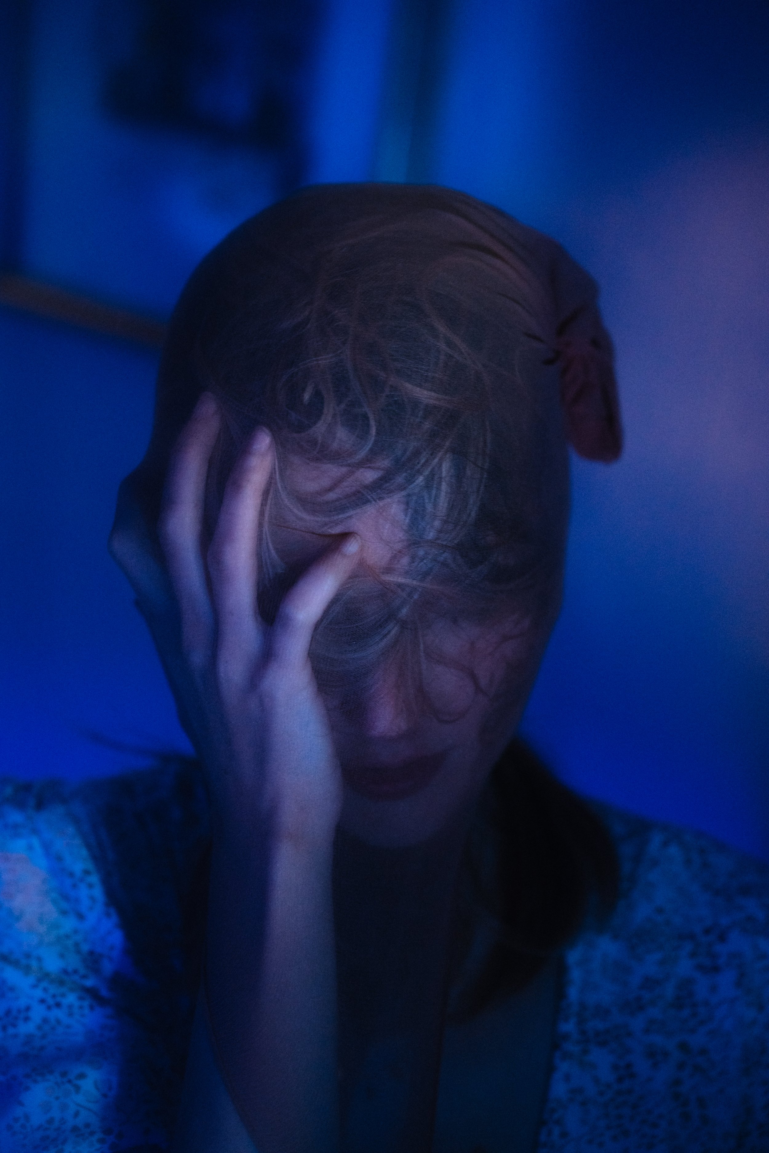 Une femme avec des cheveux bouclés et longs, tenant son visage avec une main, dans un éclairage bleu foncé et sombre.
