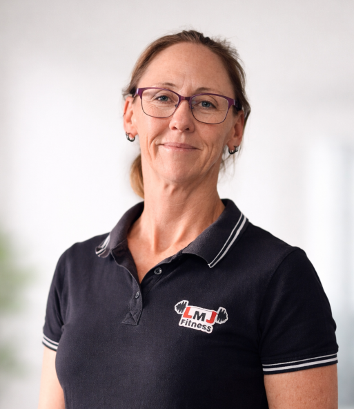 A woman with glasses and earrings wearing a black polo shirt with white trim and a logo that reads 'LMJ Fitness' on the left side, smiling softly against a plain background.