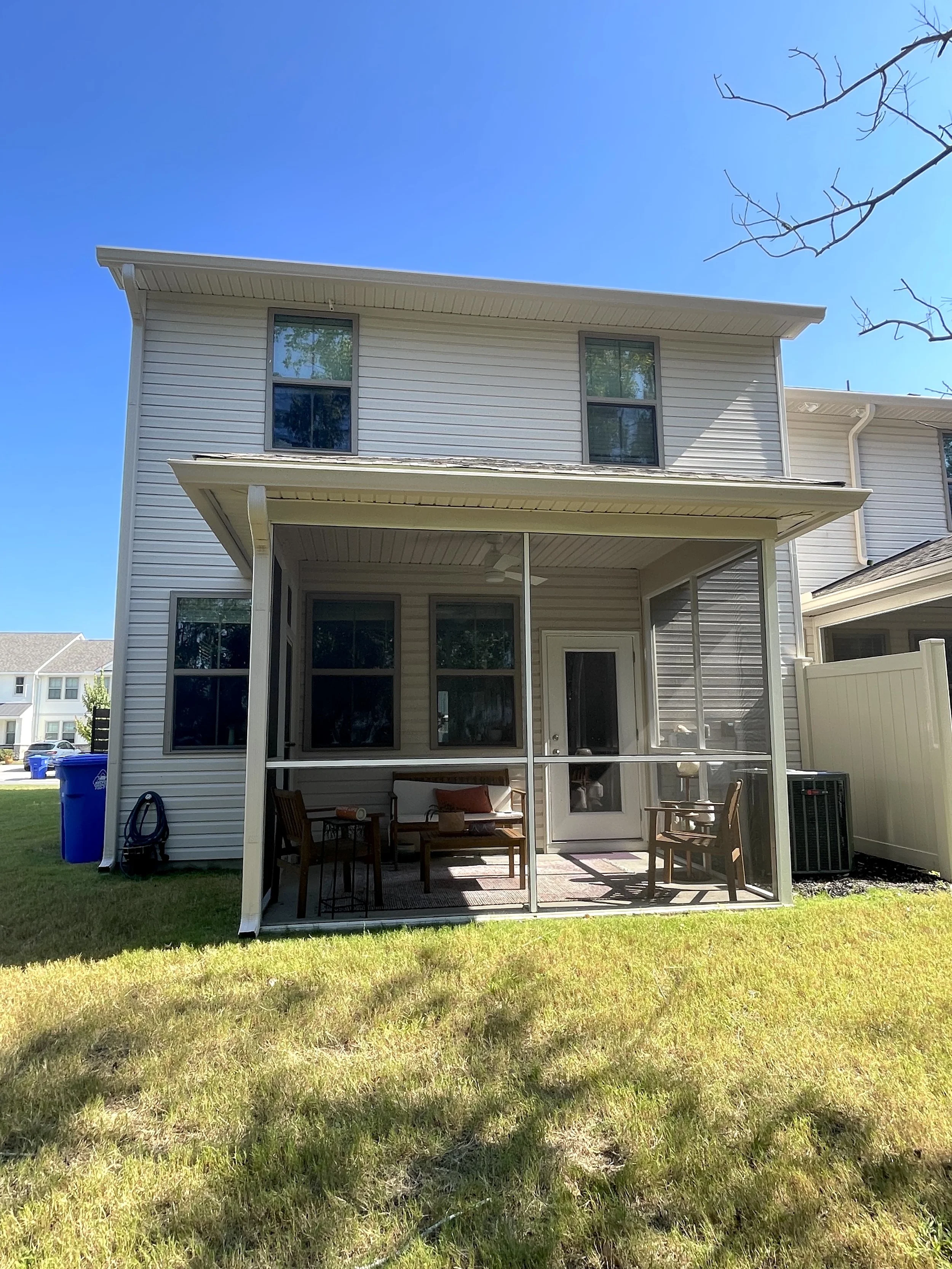The image shows a two-story house with a screened porch, lawn in the foreground, and a clear blue sky above.