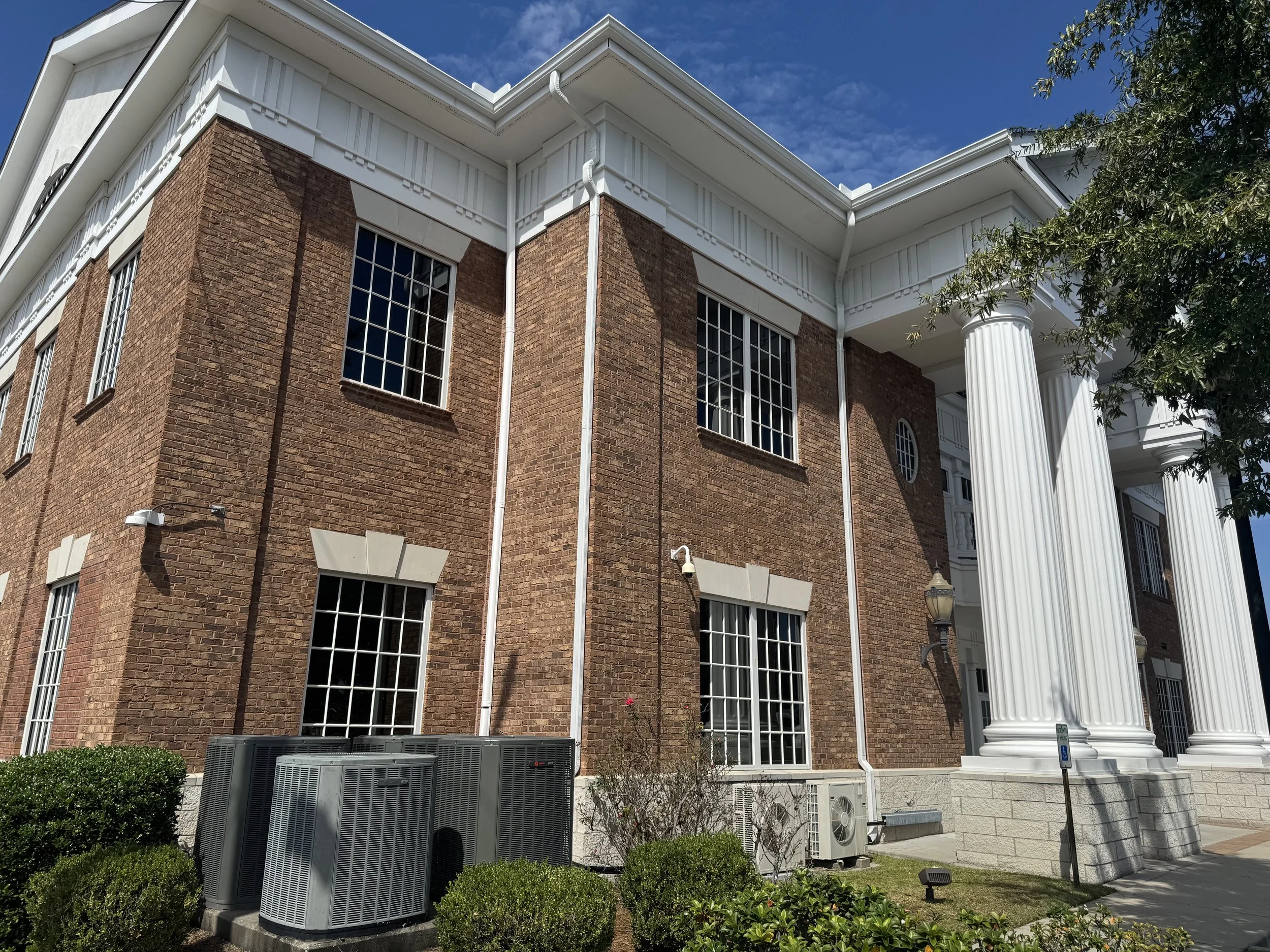 A brick building with large white columns and multiple windows under a blue sky with some clouds.