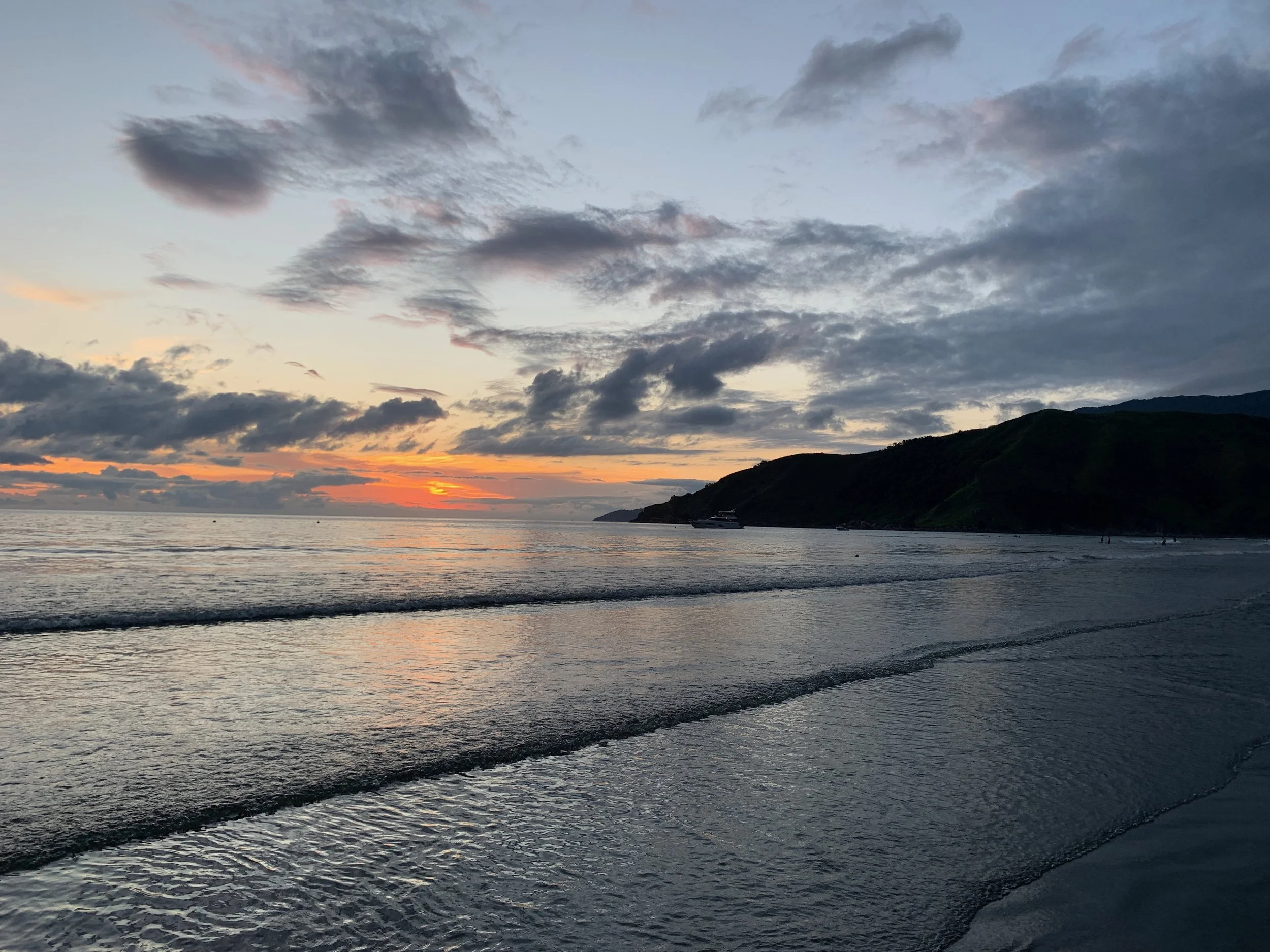 Sunset over the ocean with a partly cloudy sky and hills in the distance.