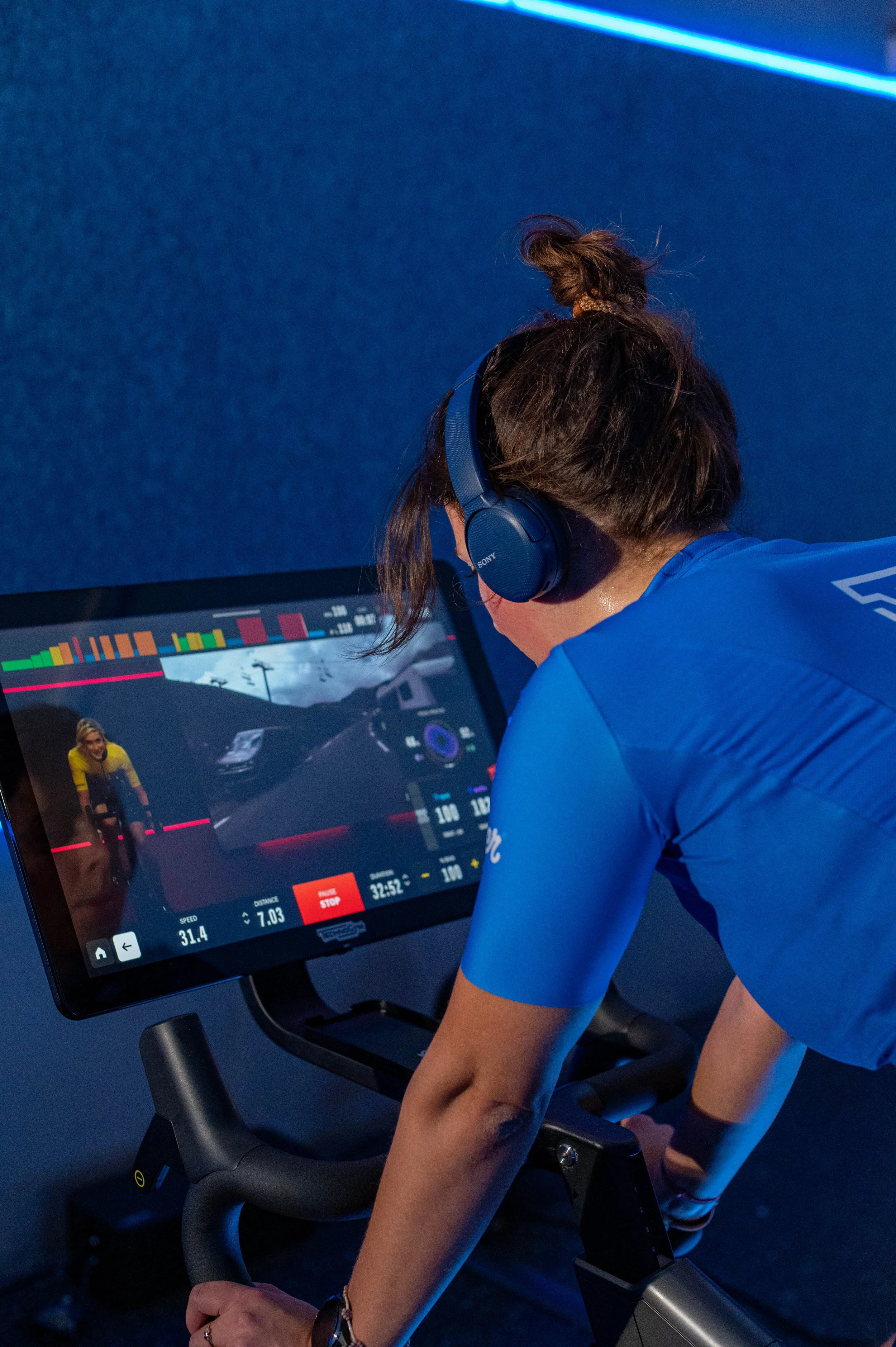 Vrouw die op een hometrainer fietst terwijl ze naar een scherm kijkt dat haar trainingsgegevens toont.