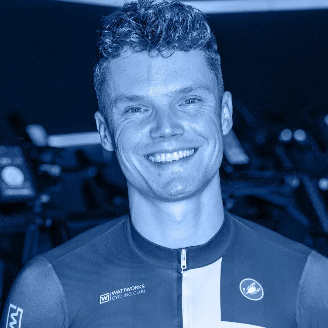 Een glimlachende man in een wielrenoutfit met het logo van Wattworks Cycling Club, achtergrond met fietsen.