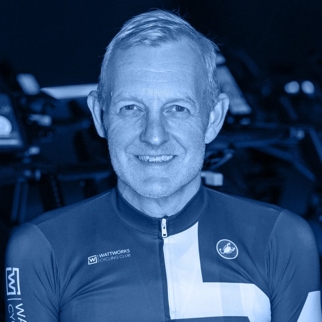 Een oudere man met grijs haar en een glimlach, gekleed in een wielrenshirt met logo's van Wattworks en Løv Cycling.