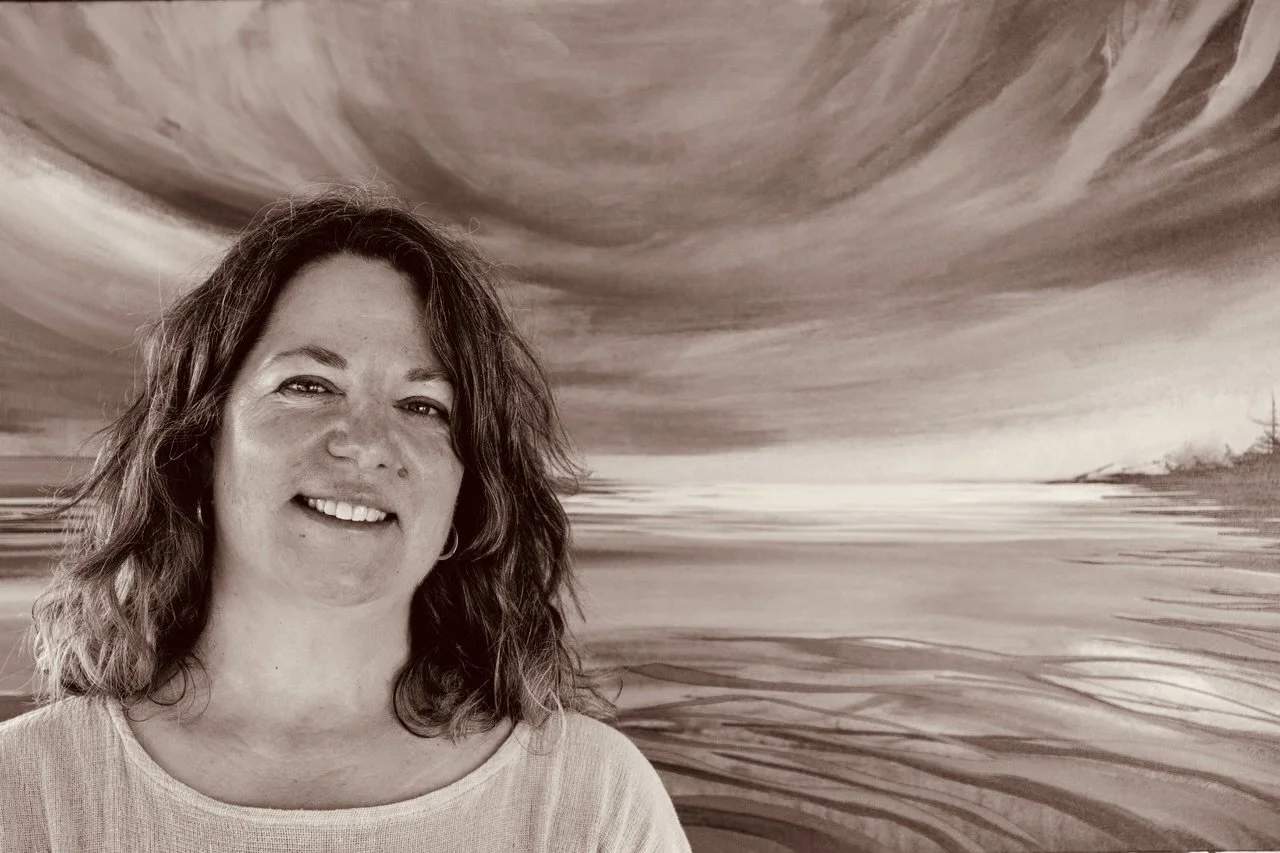 Mary Loos  with wavy hair smiling in front of an abstract river painting with swirling patterns.