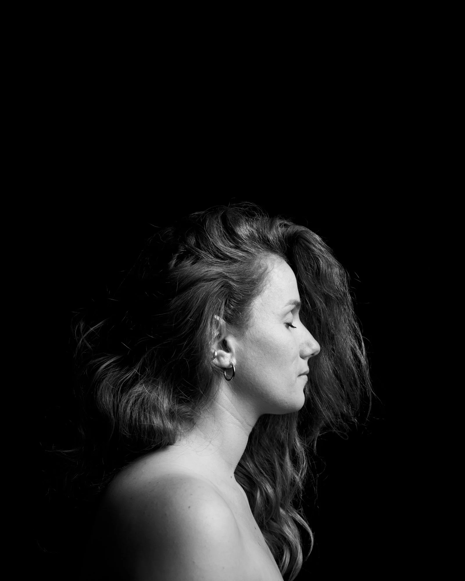 Dramatic low-key lighting portrait of a person with eyes closed in a calm pose.