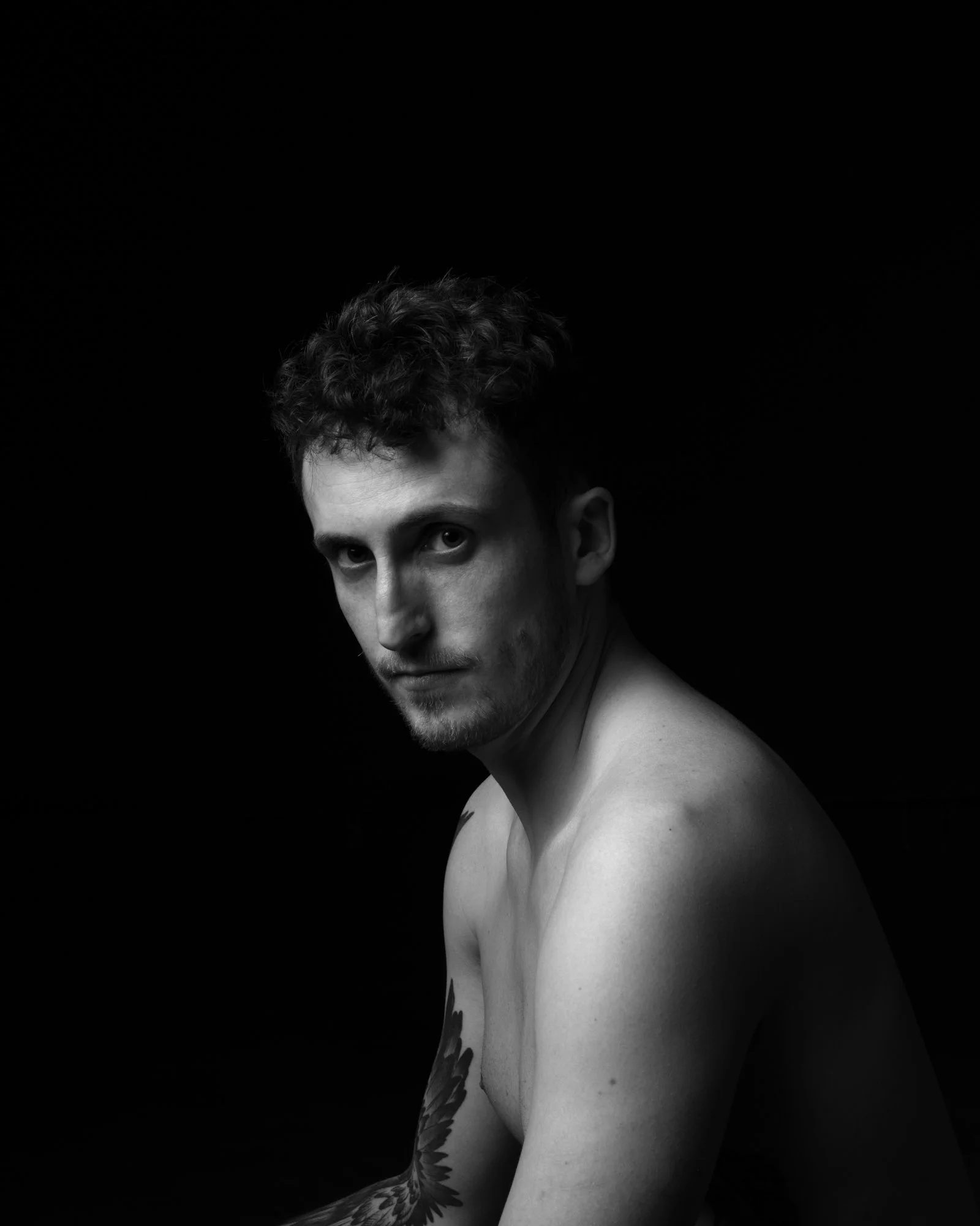 Dramatic three-quarter profile portrait with intense, focused chiaroscuro lighting.