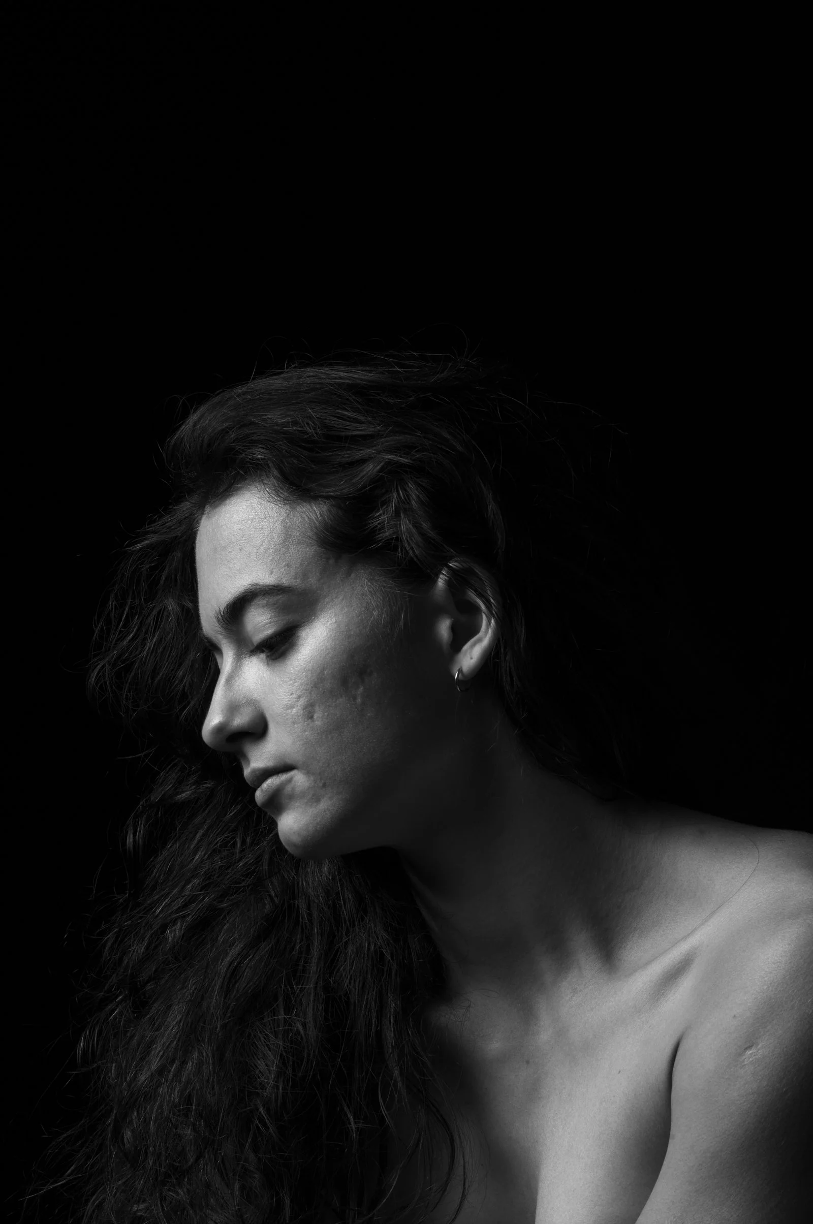 Chiaroscuro style portrait emphasizing a single focused light source and deep blacks.
