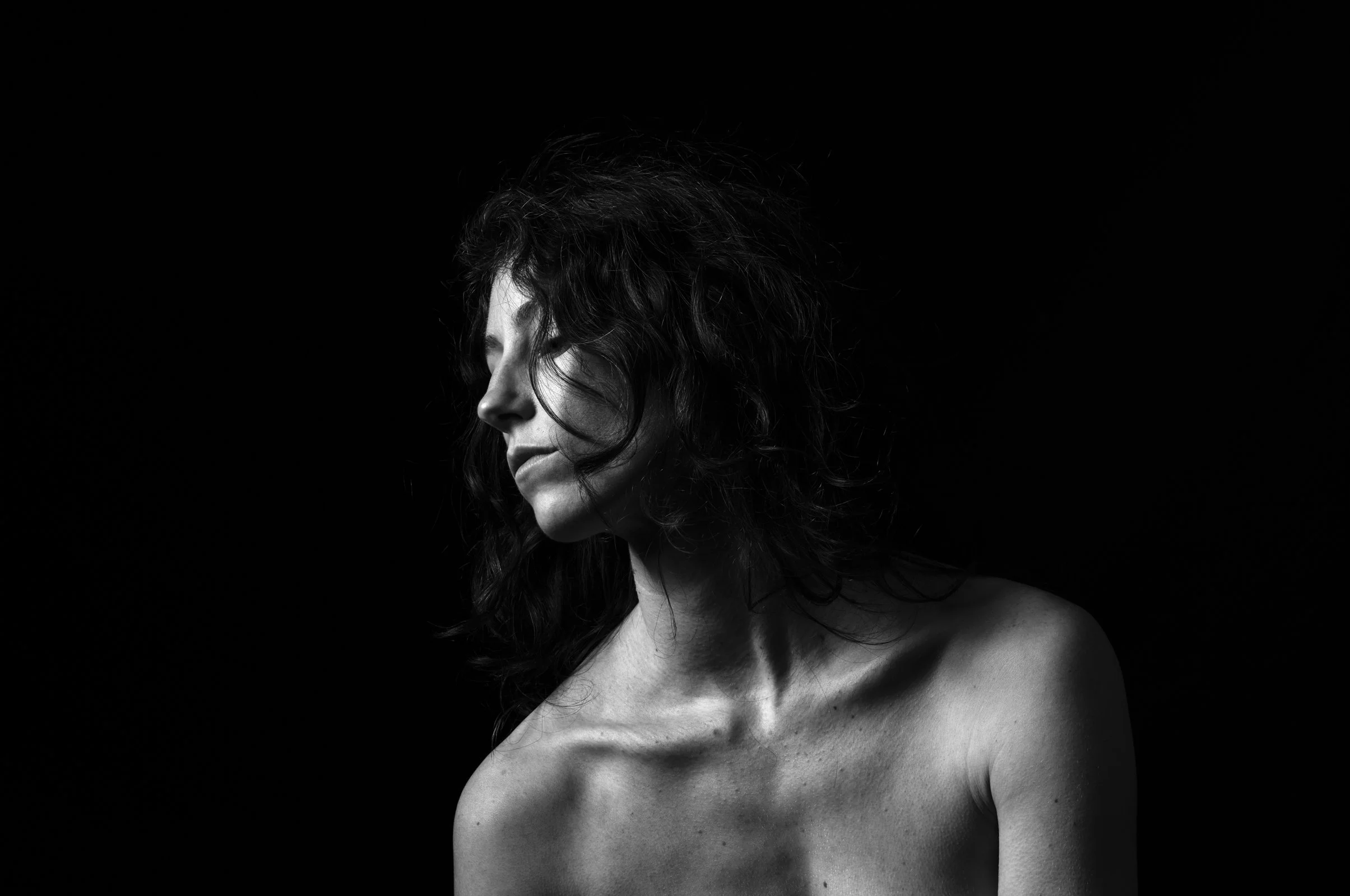 Chiaroscuro portrait of a figure in motion, partially veiled by intense dark shadows.