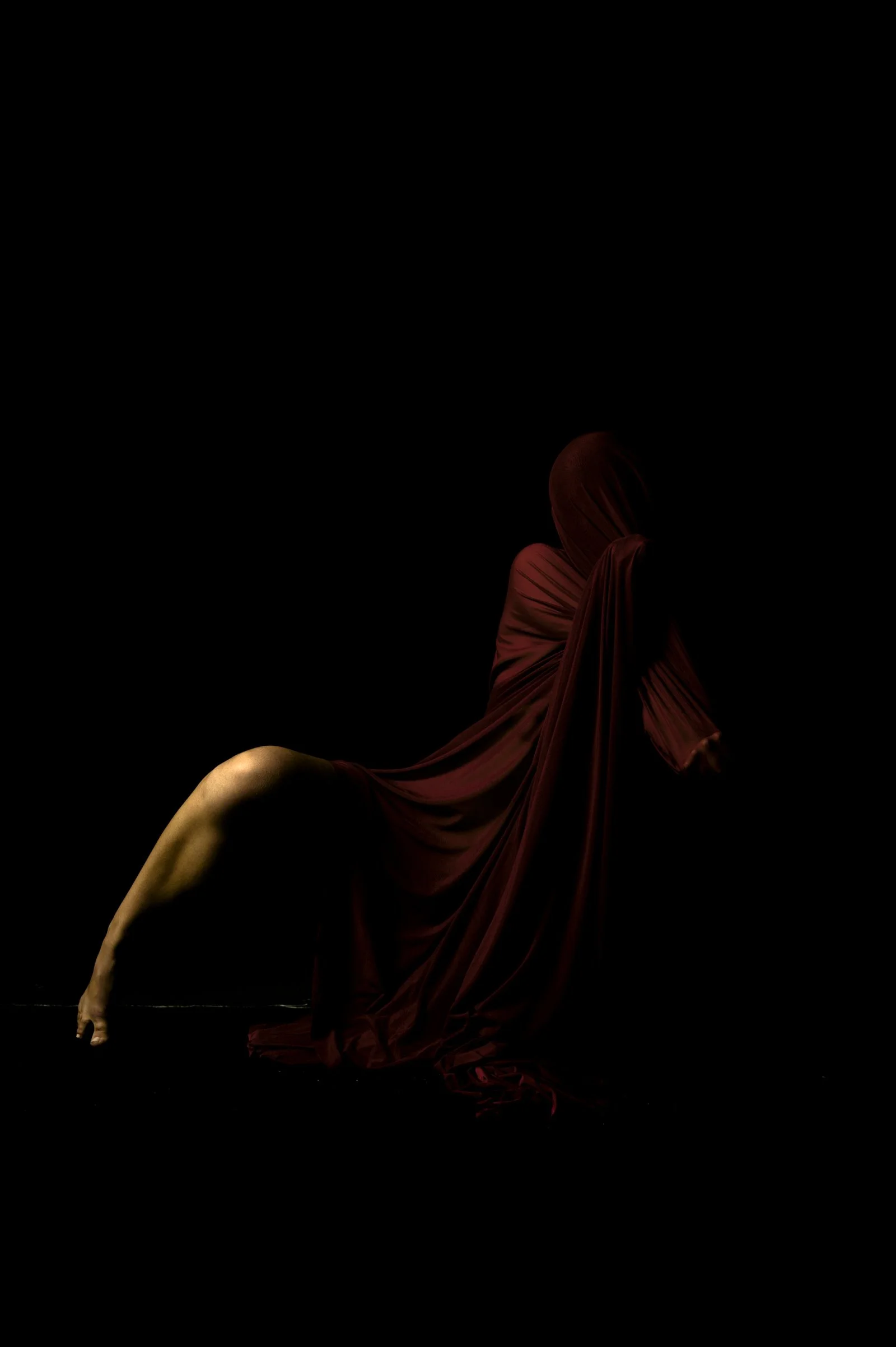 Subtle light catching the edges of a red drape and the human form beneath.