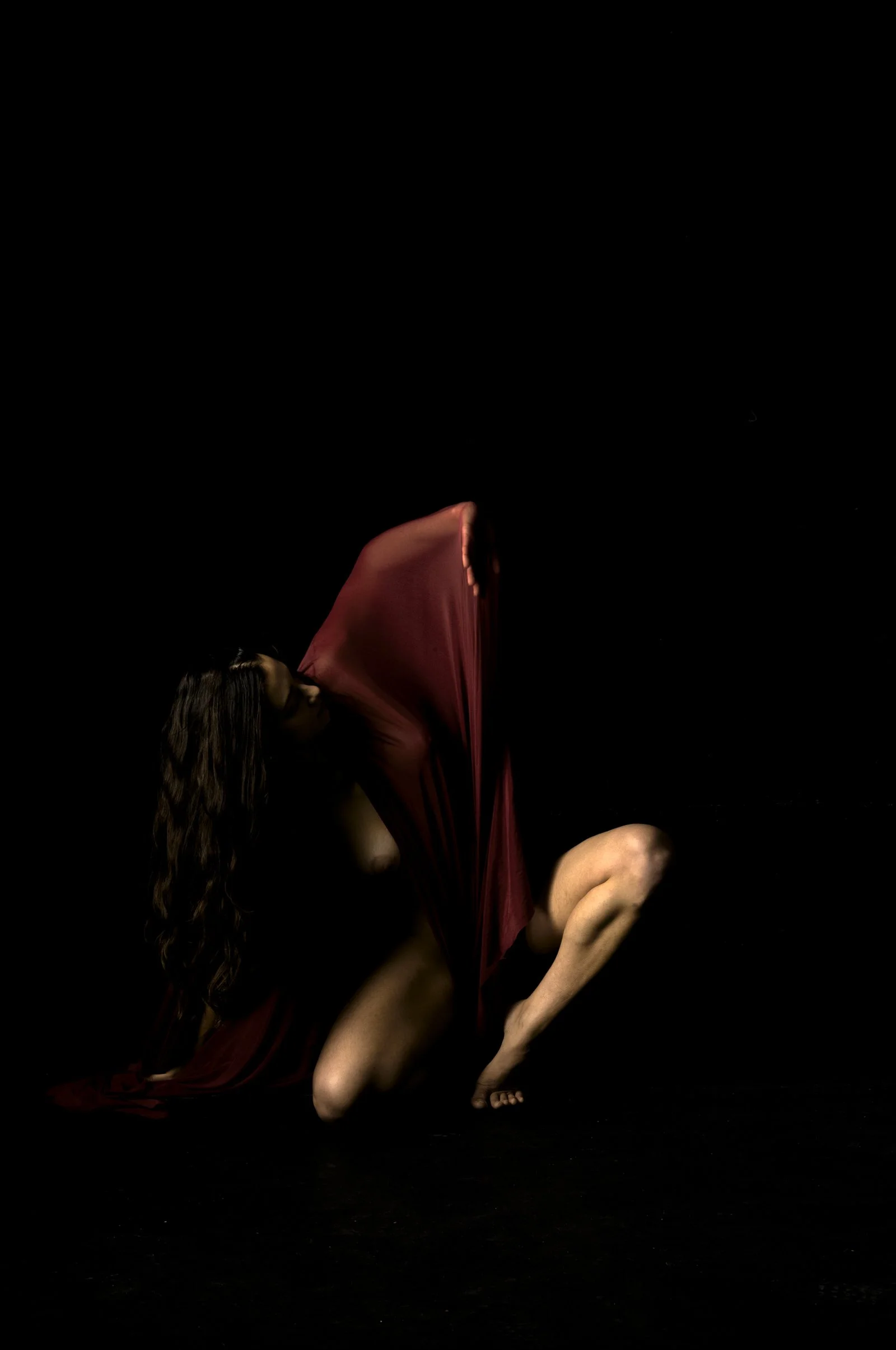 Fine art portrait of a subject in motion, covered by a translucent red cloth.