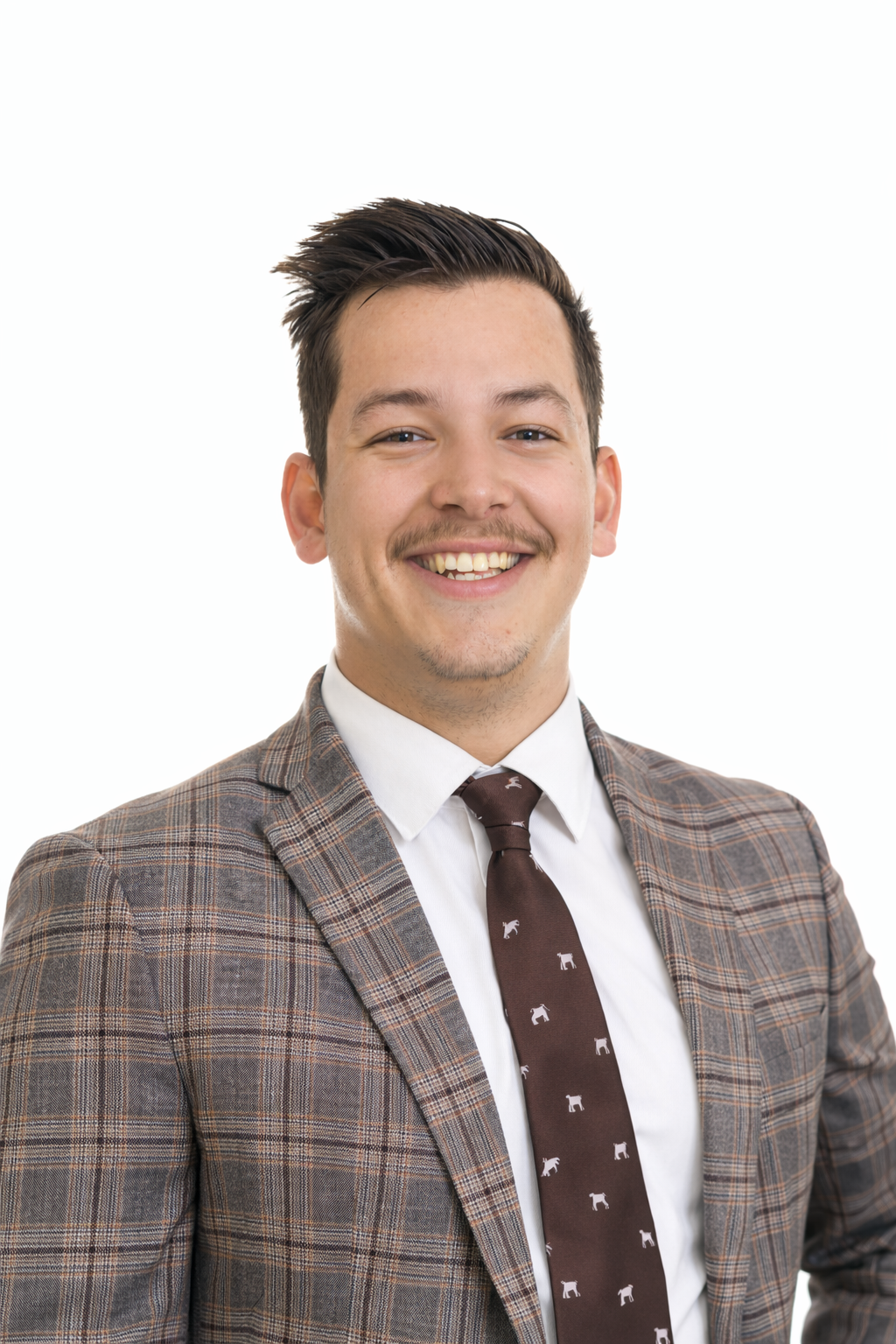 Un homme souriant habillé en costume à carreaux, chemise blanche et cravate marron avec des motifs d'éléphants, sur fond blanc.