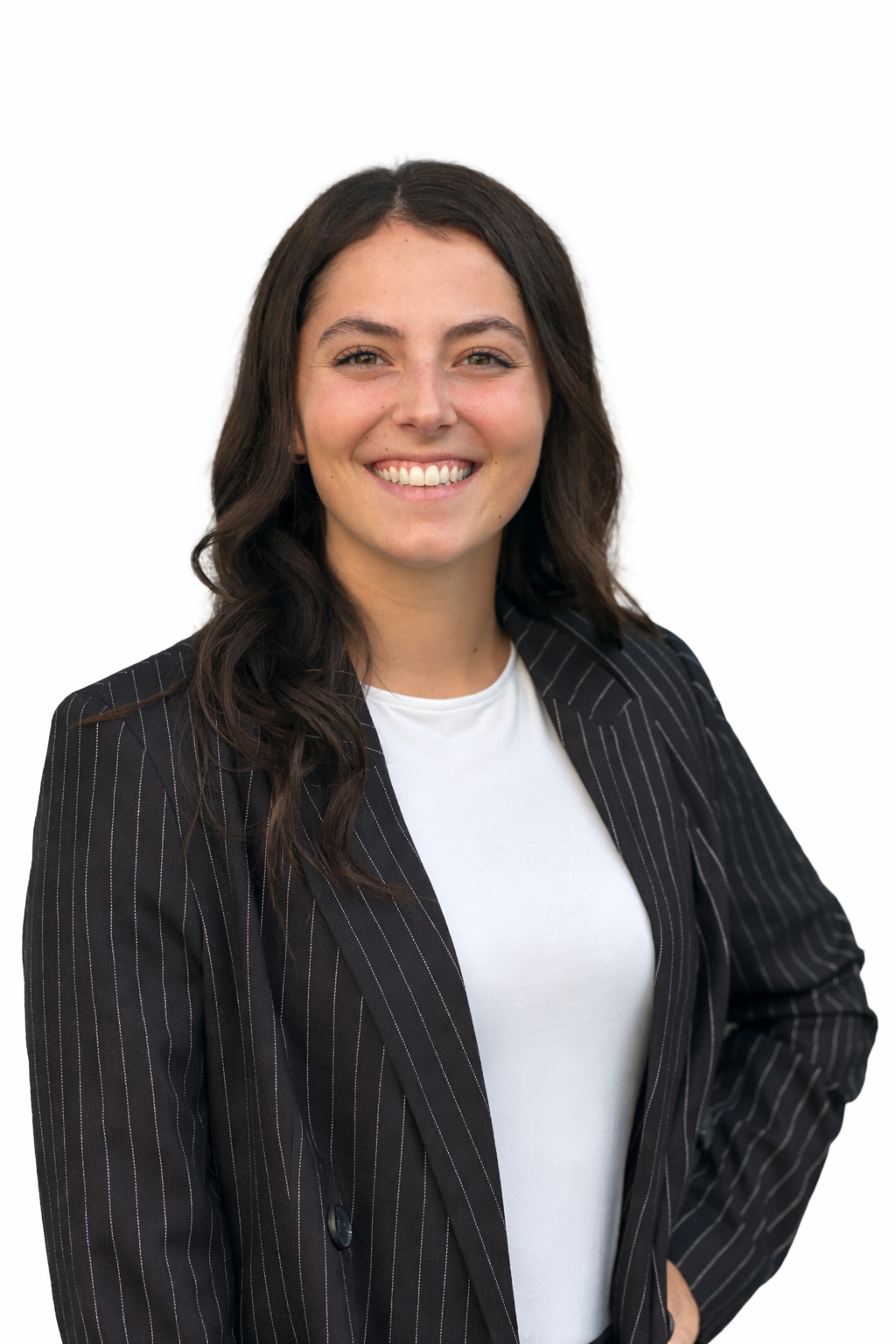 Une femme souriante avec des cheveux bruns, portant un blazer rayé et une chemise blanche, pose contre un fond blanc.
