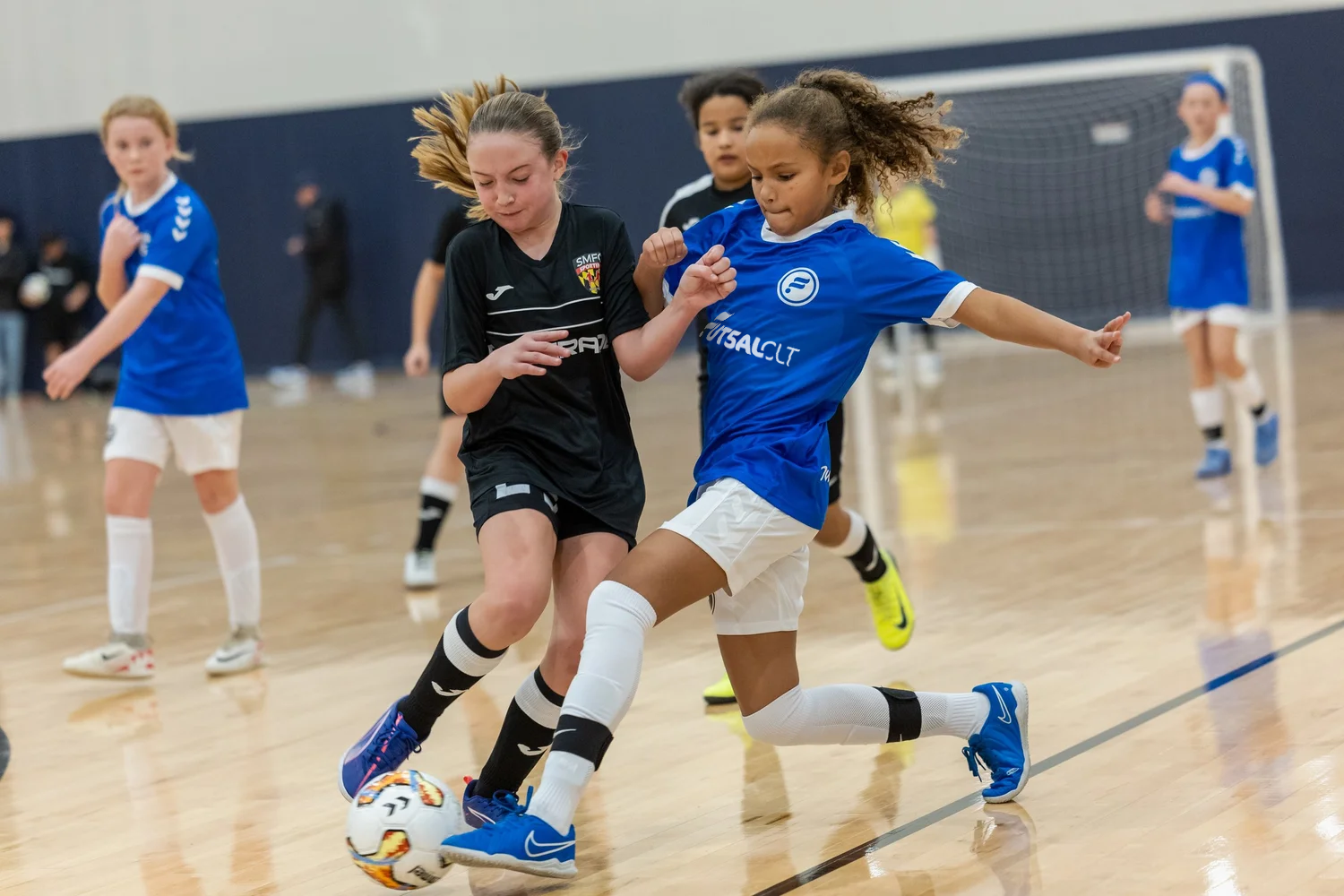 Young girls playing indoor Futsal, two girls contesting for the ball on the court.