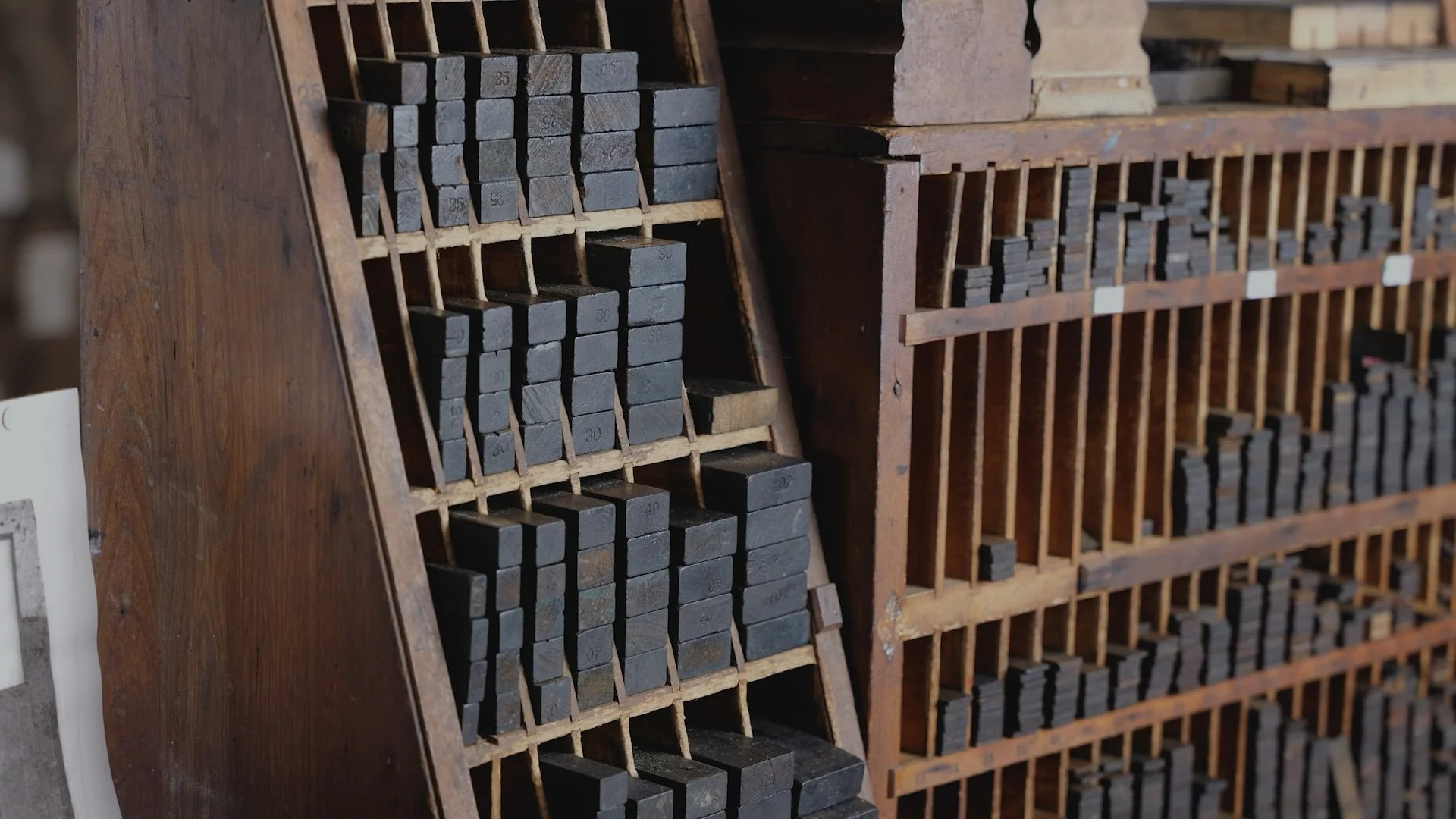 Close-up of a wooden storage rack filled with small metal blocks, each labeled with a number, in a workshop or hardware store.