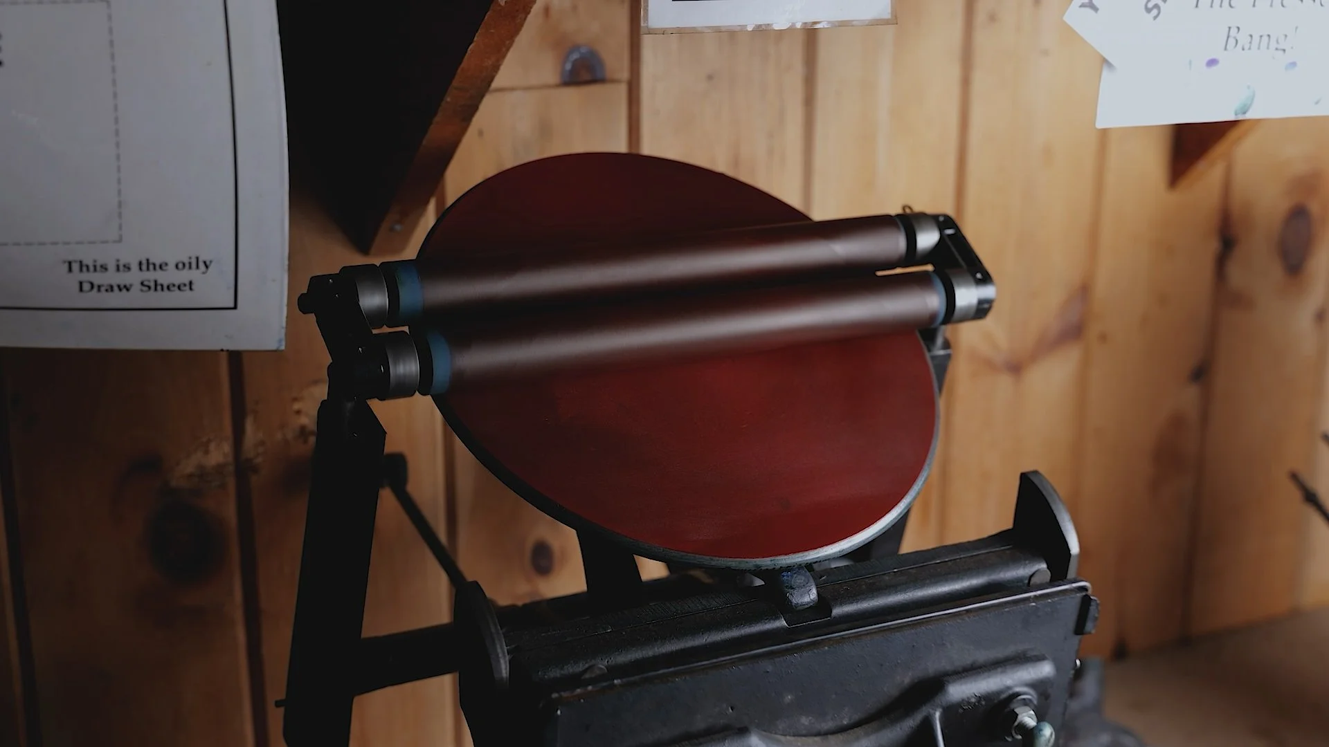 A vintage mimeograph machine with wooden rollers and a flat red surface.