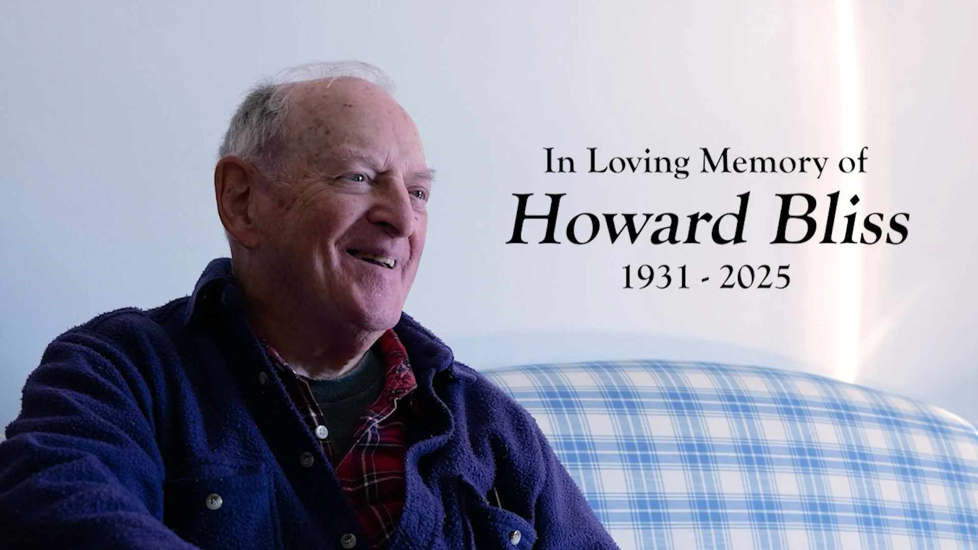 A smiling elderly man with white hair and a blue fleece jacket sitting on a plaid armchair, with text honoring Howard Bliss, 1931-2025, in loving memory.
