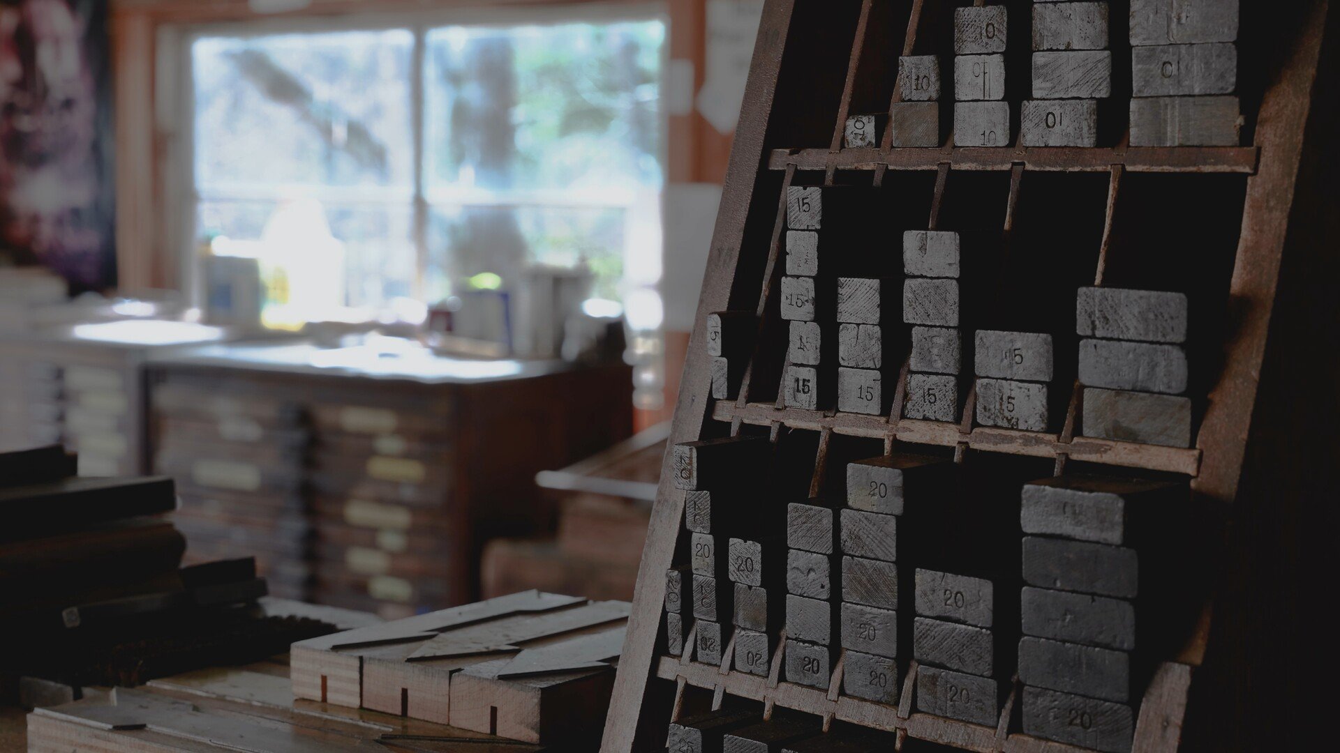 Close-up of a vintage wooden printing block display with numbered gray blocks, with a blurred workshop background.
