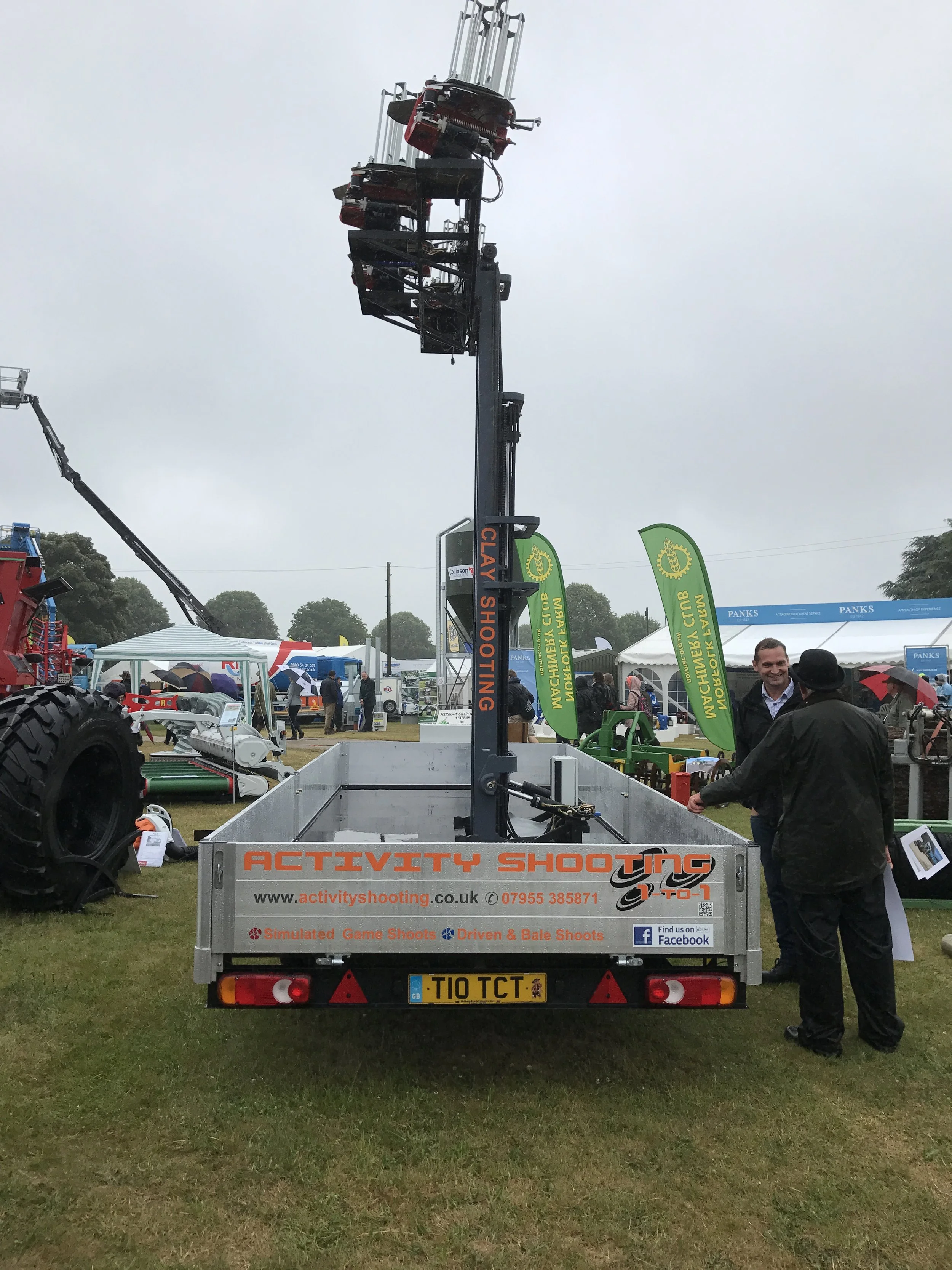A mobile shooting range vehicle labeled 'Activity Shooting' with a large mechanical arm for simulated game shooting, displayed at an outdoor event with tents and people around.