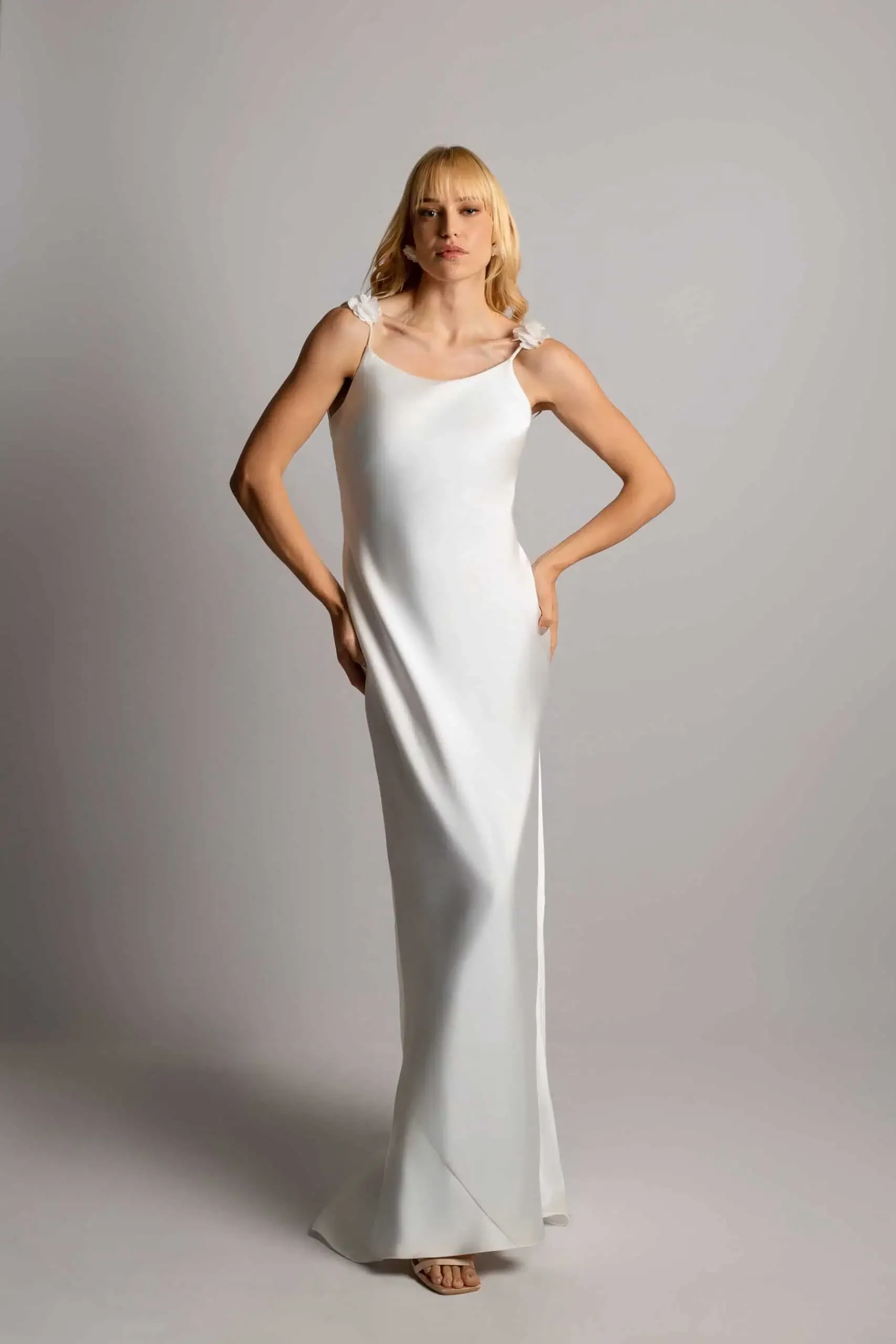 A woman in a long white dress standing against a plain background.