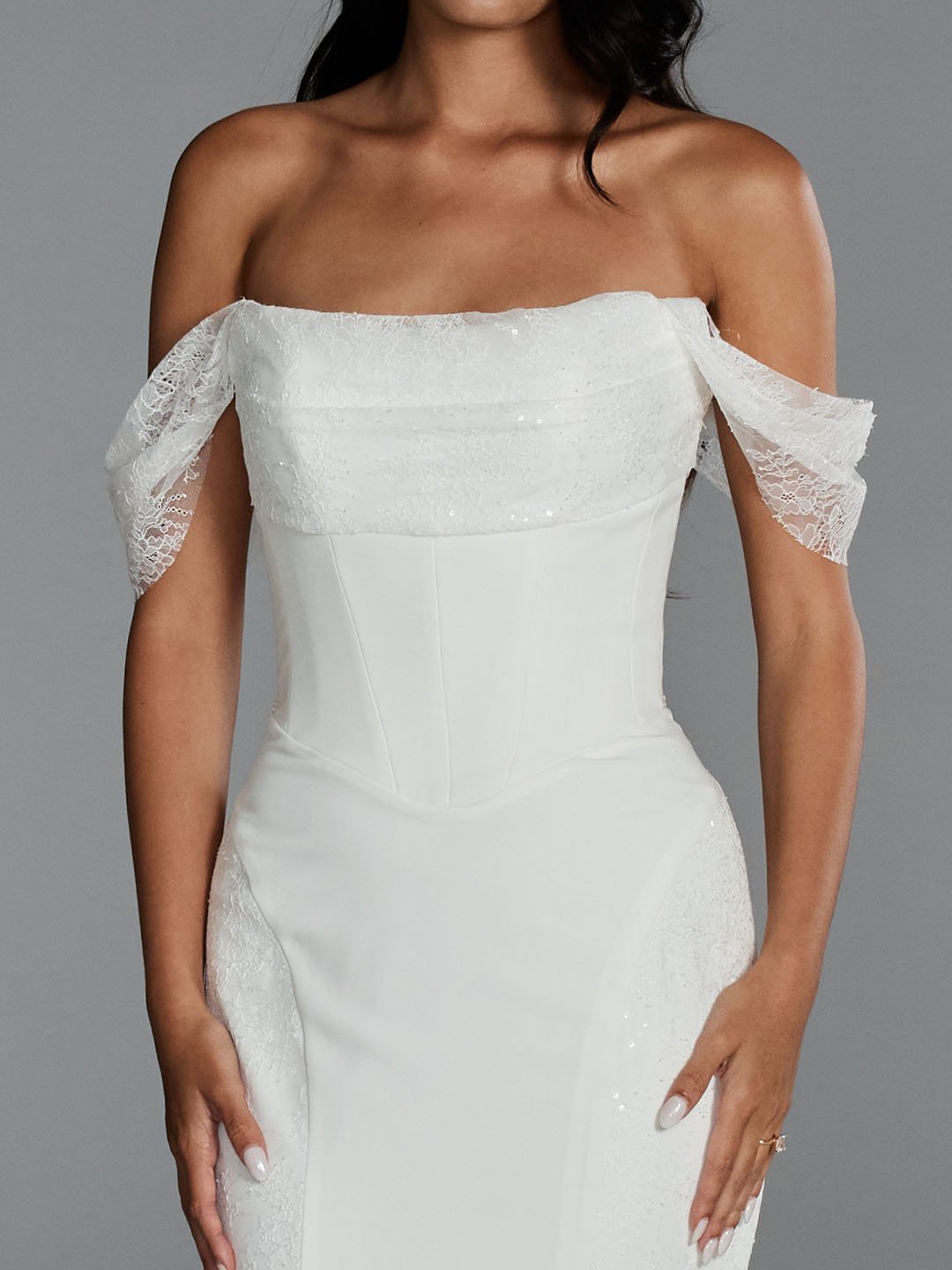 A woman wearing an elegant white off-the-shoulder dress with lace sleeves and a fitted bodice.