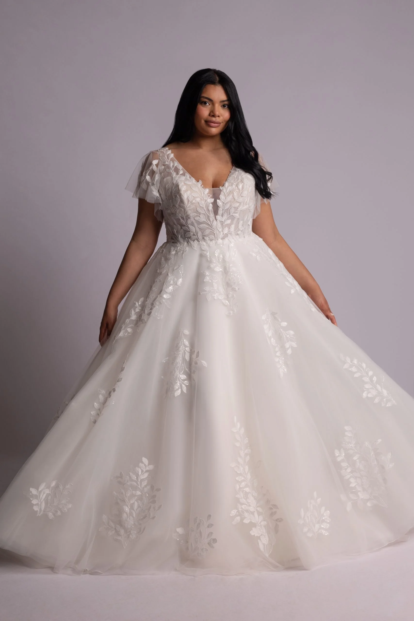 Woman wearing a white wedding dress with floral embroidery and tulle appliqué details.