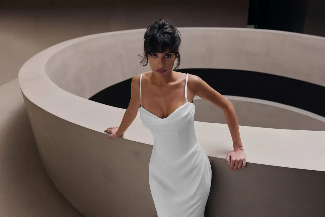 A woman in a white dress leaning on a curved beige balcony railing.