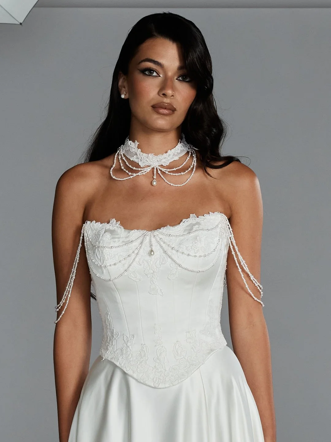 A woman wearing an elegant white wedding gown with pearl and lace jewelry accessory.