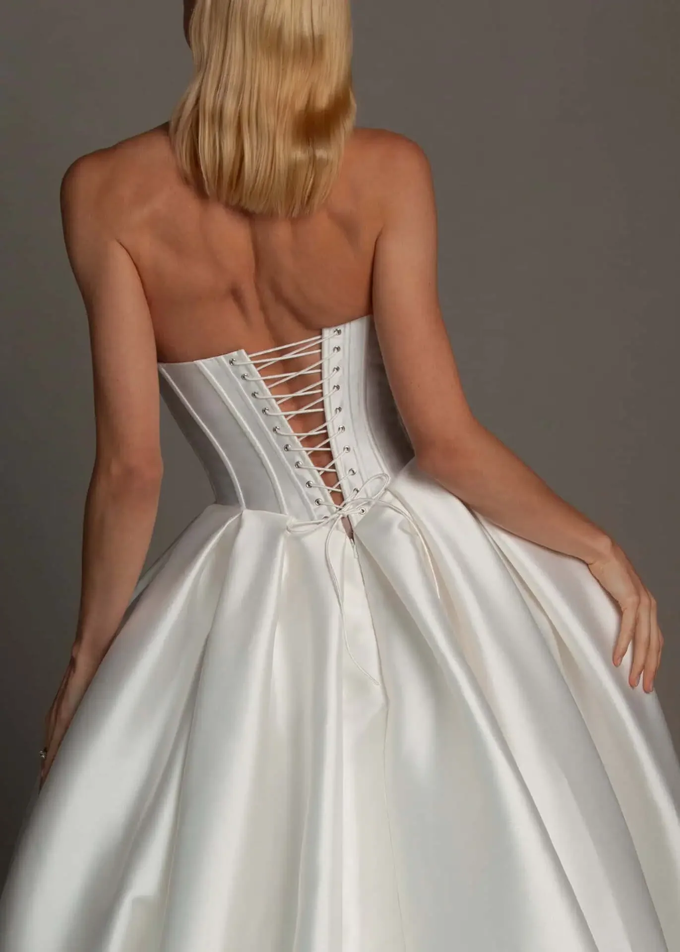 Back view of a woman in a white, strapless, satin ball gown with a corset back laced up.