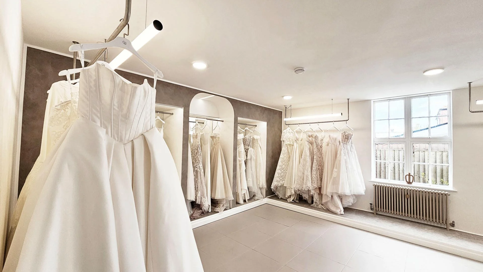 Wedding dress shop with white wedding gowns on racks, a large window, and neutral-colored walls.