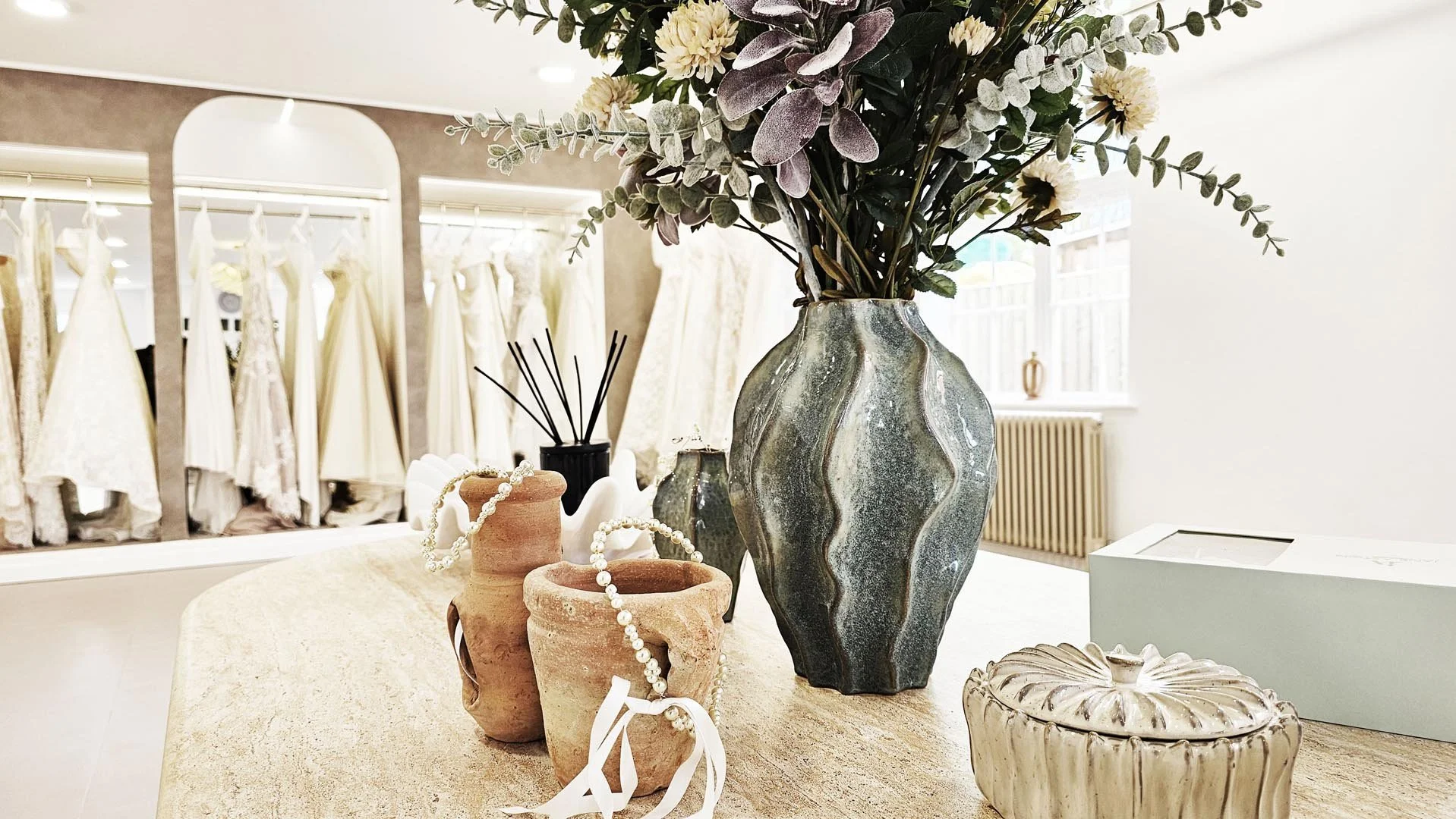 Decorative vases and jewelry on a table with wedding dresses in the background.