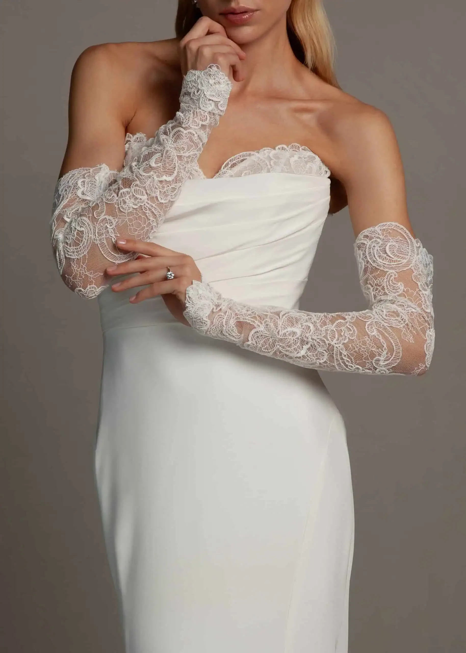 A woman wearing a white strapless wedding dress with lace off-the-shoulder sleeves.