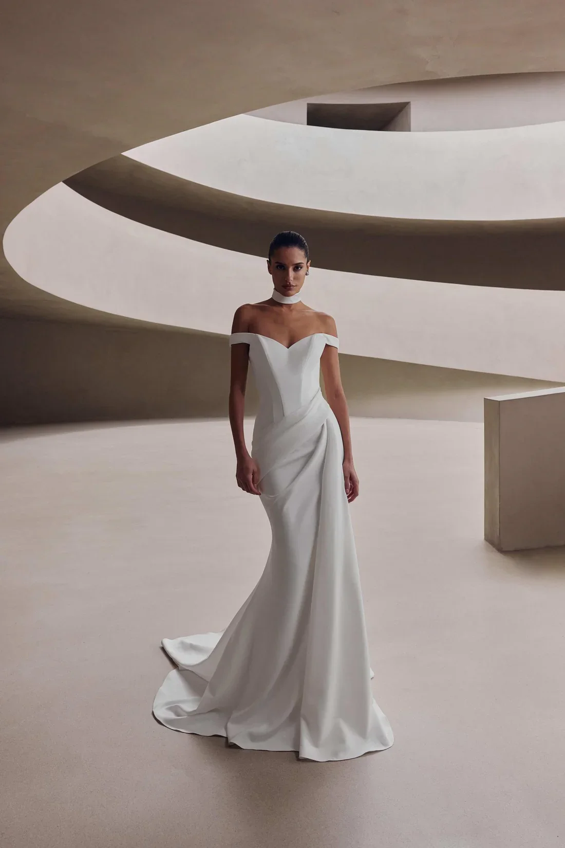 A woman in a white wedding dress standing indoors with modern architecture in the background.