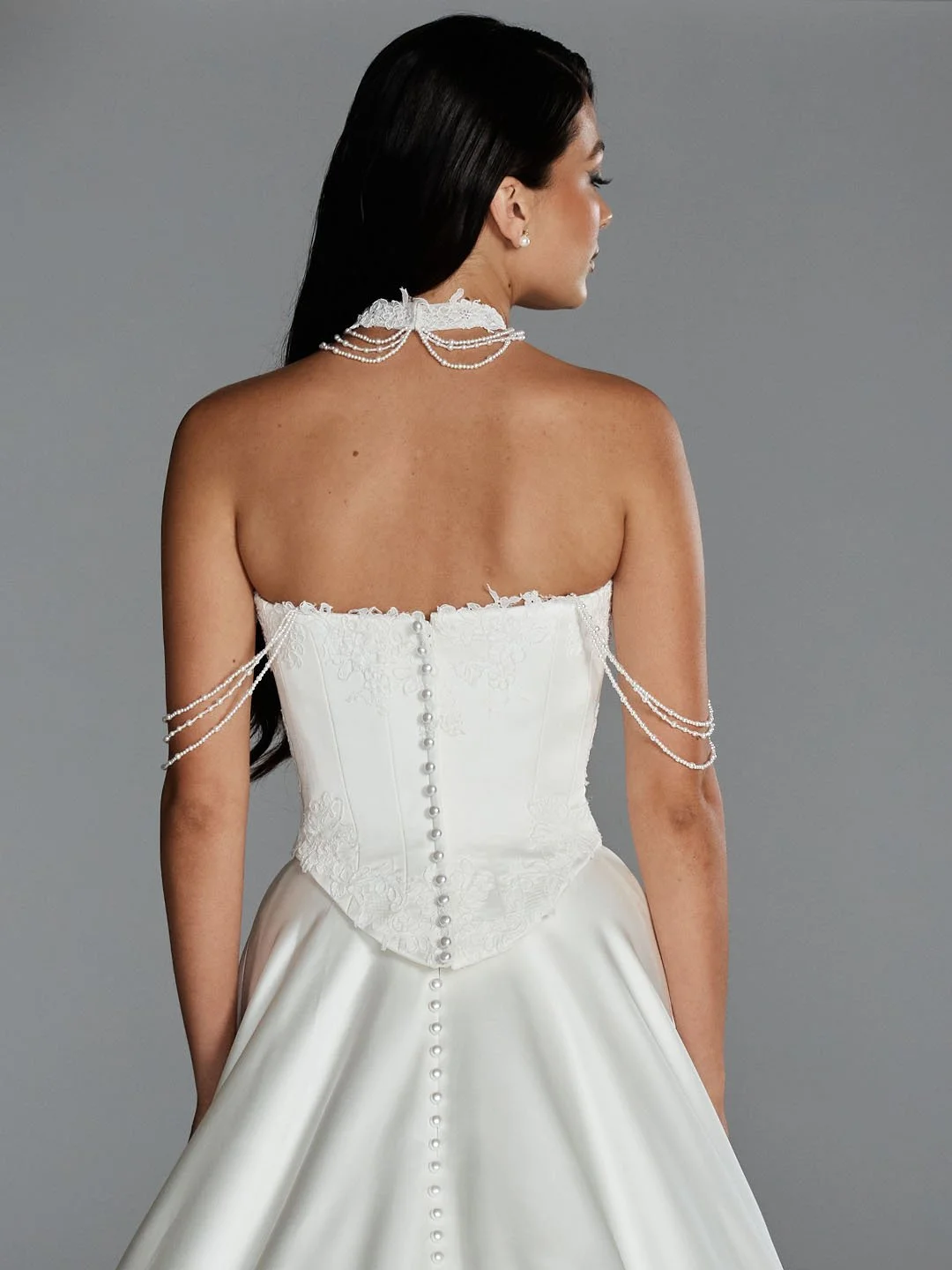 Back of a woman in a white wedding dress with pearl embellishments and jewelry.