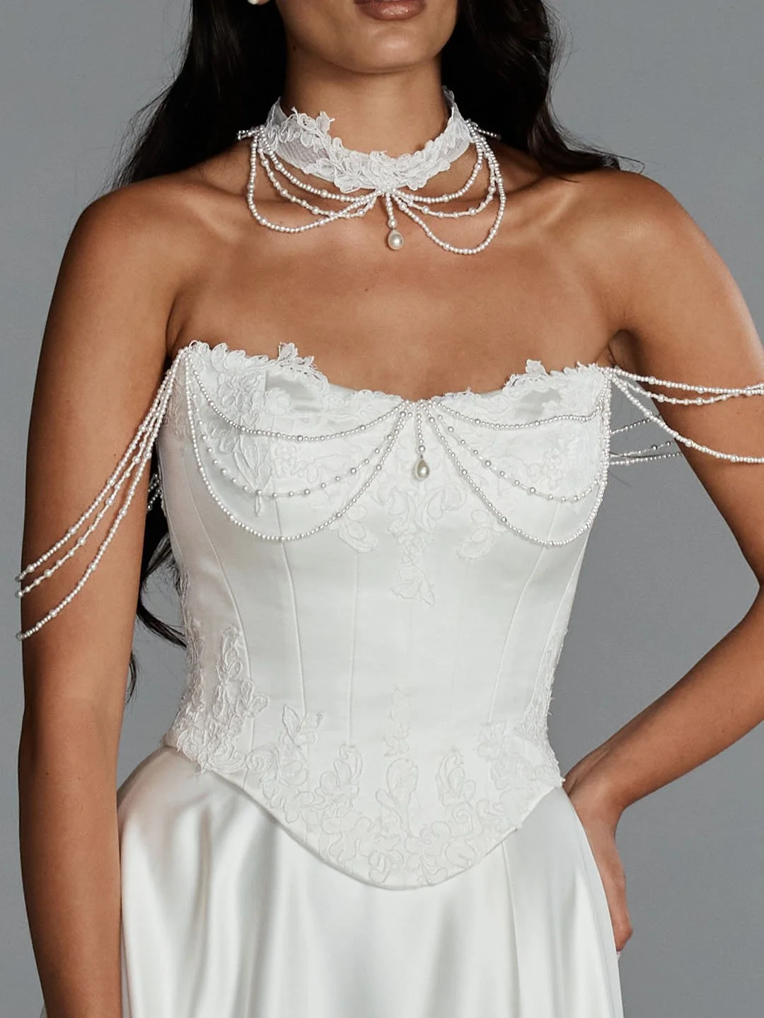 A woman wearing a white wedding dress with intricate embroidery, pearl necklace with multiple strands, and pearl embellishments on the sleeves and neckline.