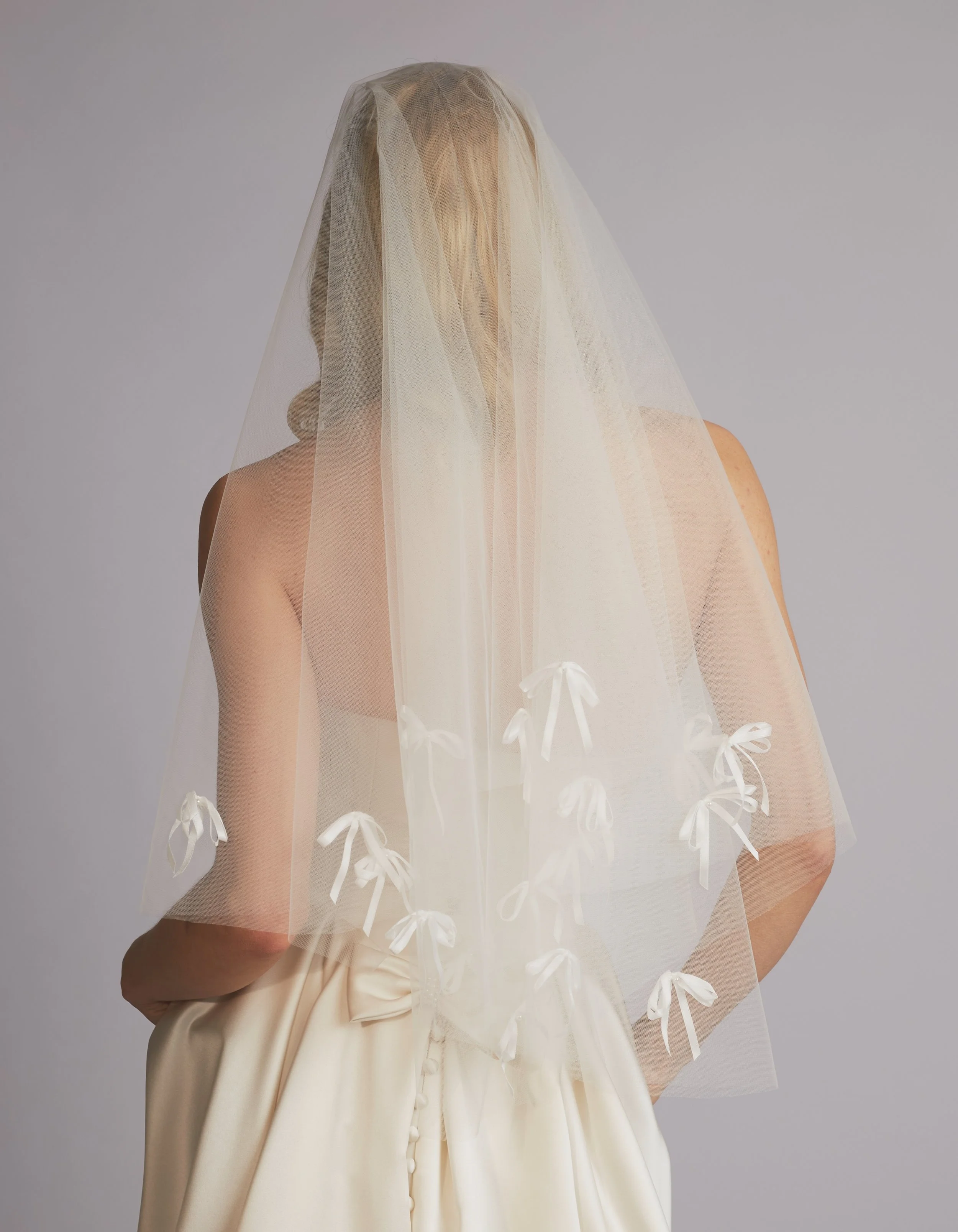 A woman in a wedding dress with a veil over her face, standing with her back to the camera.