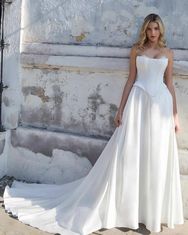A woman in a white wedding dress standing against a weathered wall.