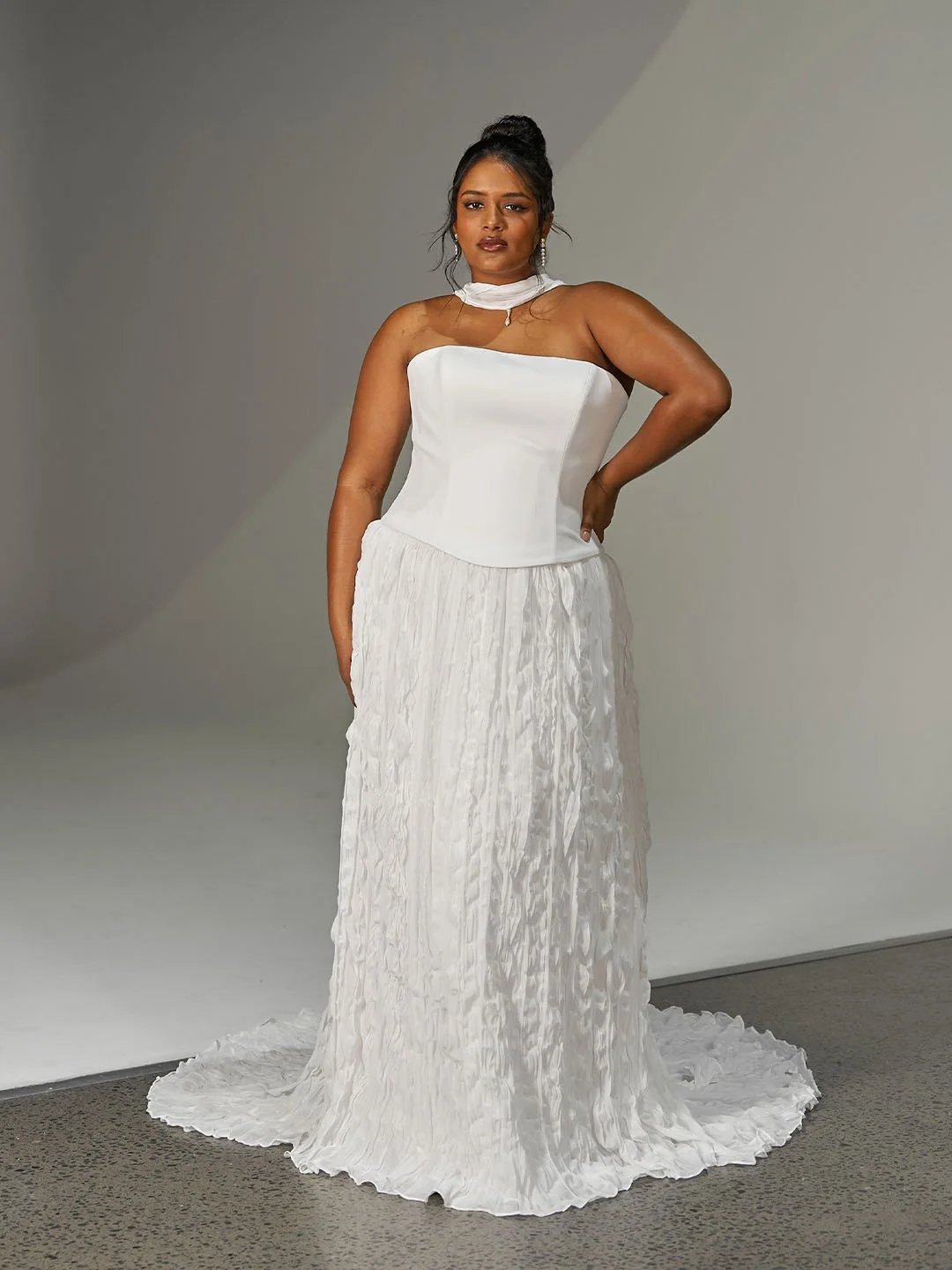 Woman in a strapless white formal gown with a fitted bodice and a long, textured skirt, standing against a neutral background.