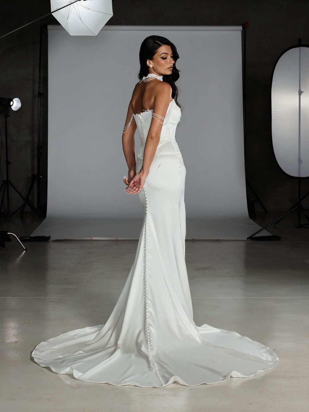 A woman in a white wedding gown with pearl embellishments in a photography studio.