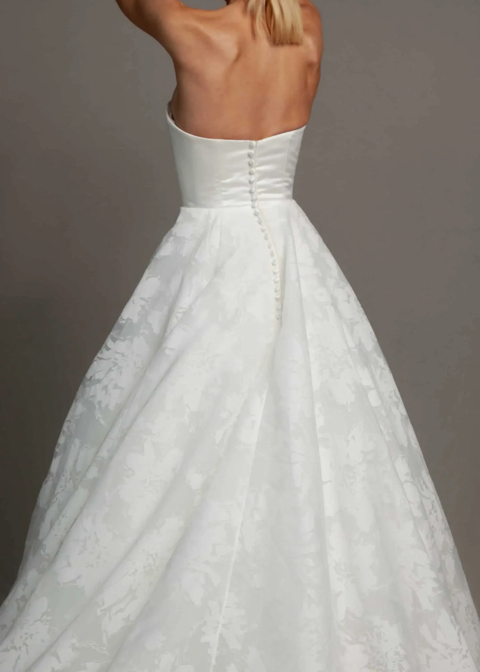 Close-up of a woman wearing a strapless white wedding gown with a textured floral pattern and a row of buttons down the back.