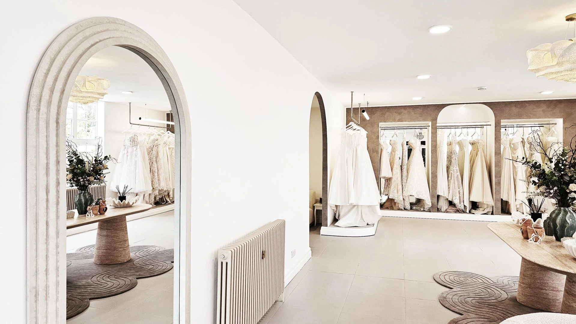 A bridal boutique with white wedding dresses hanging on racks, decorated with vases and flowers.