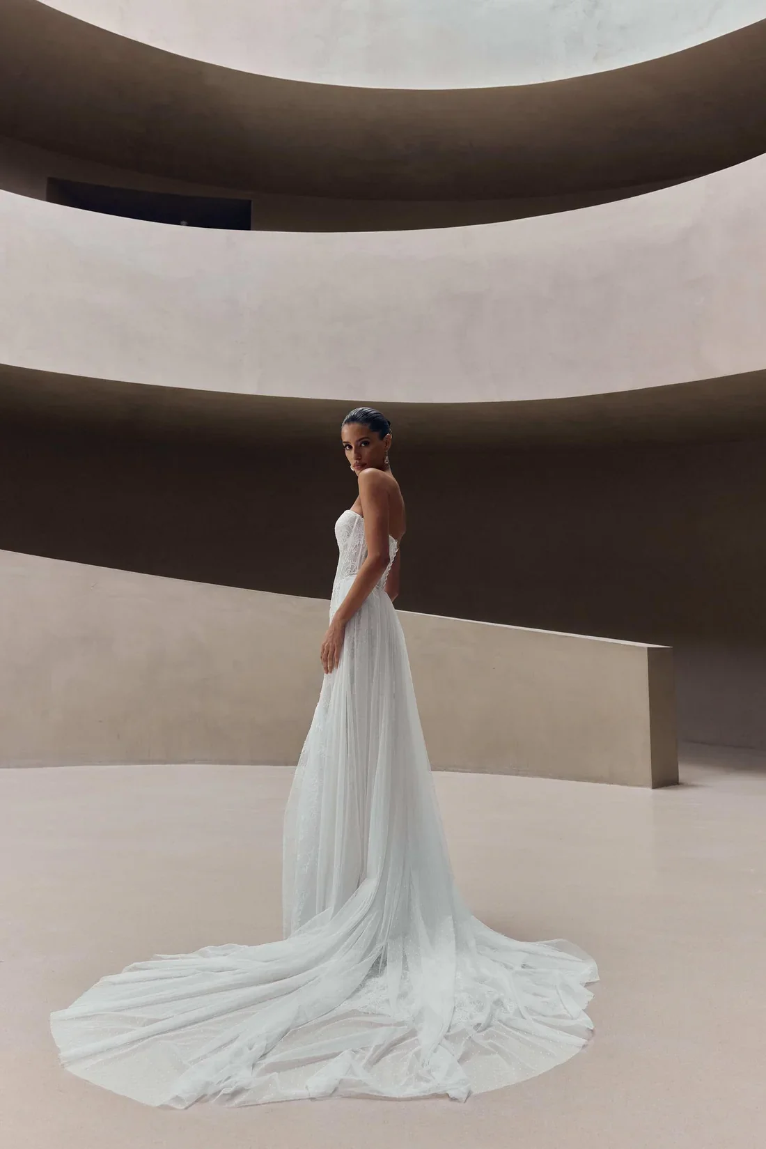 Woman in a white dress standing in a minimalist, modern architectural space with curved levels.